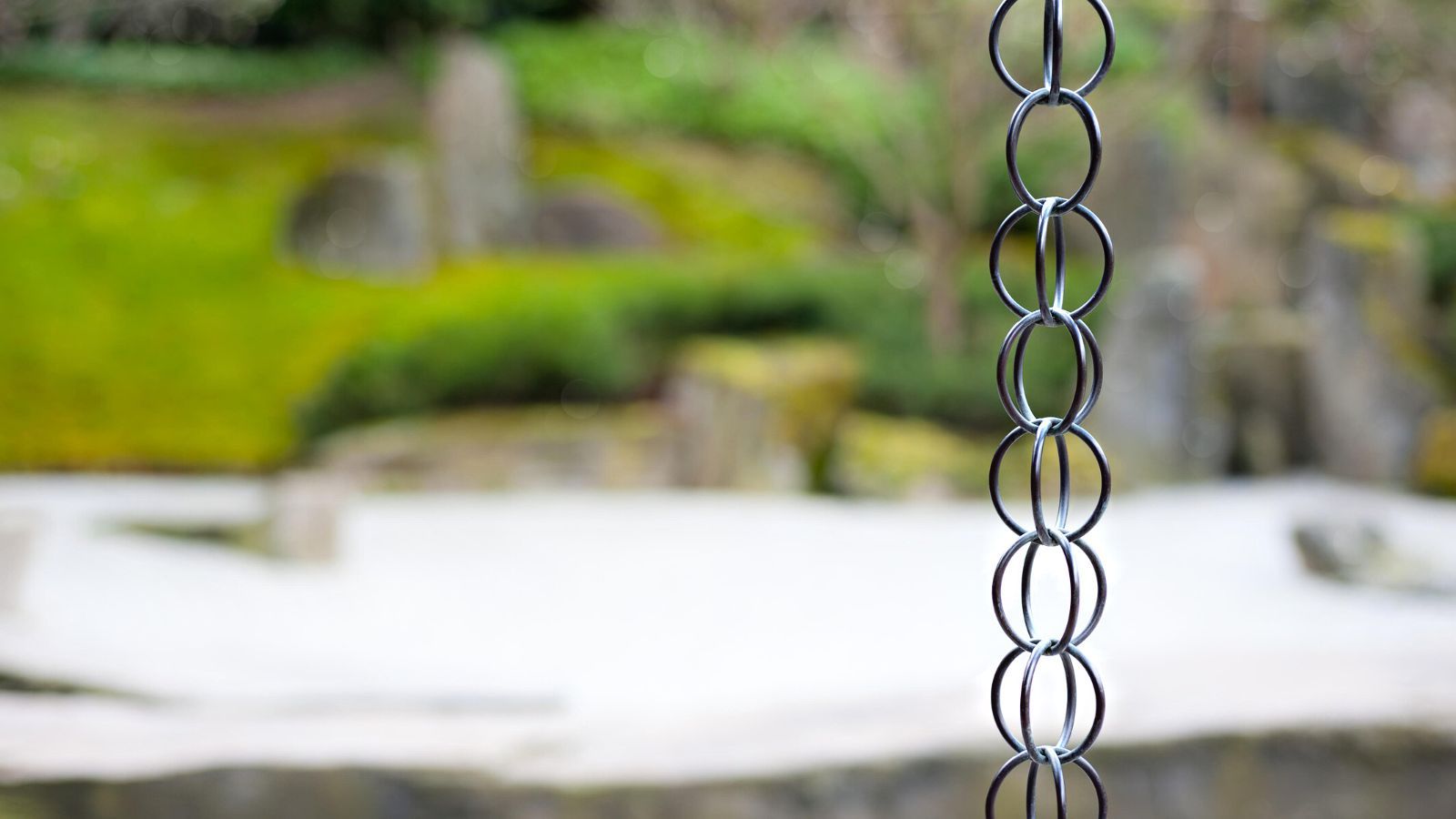 A rain chain in focus in front of a blurry garden