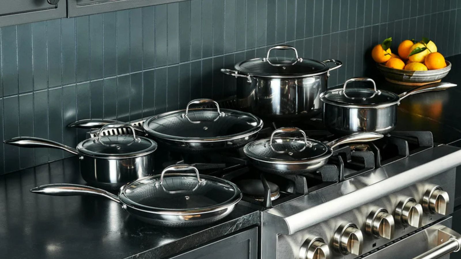 A HexClad set of 'Hybrid' pots and pans on a gas burner stove, next to a bowl of citrus fruit