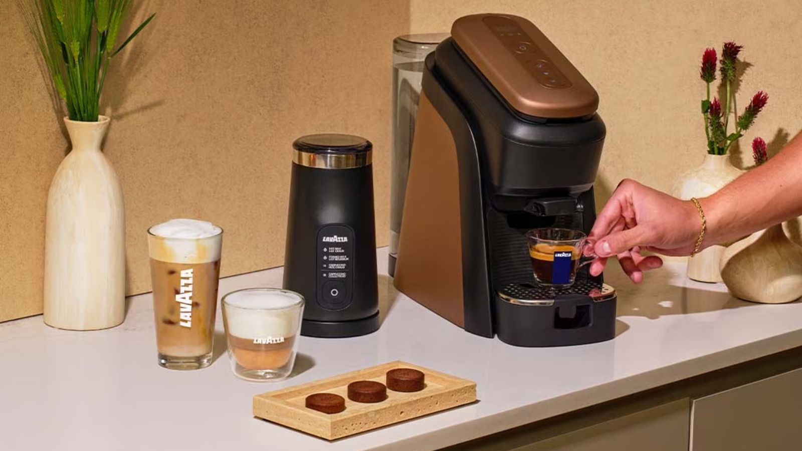 The Lavazza Tablì coffee machine in black and copper, with three no-plastic coffee tabs on a wooden tray beside it