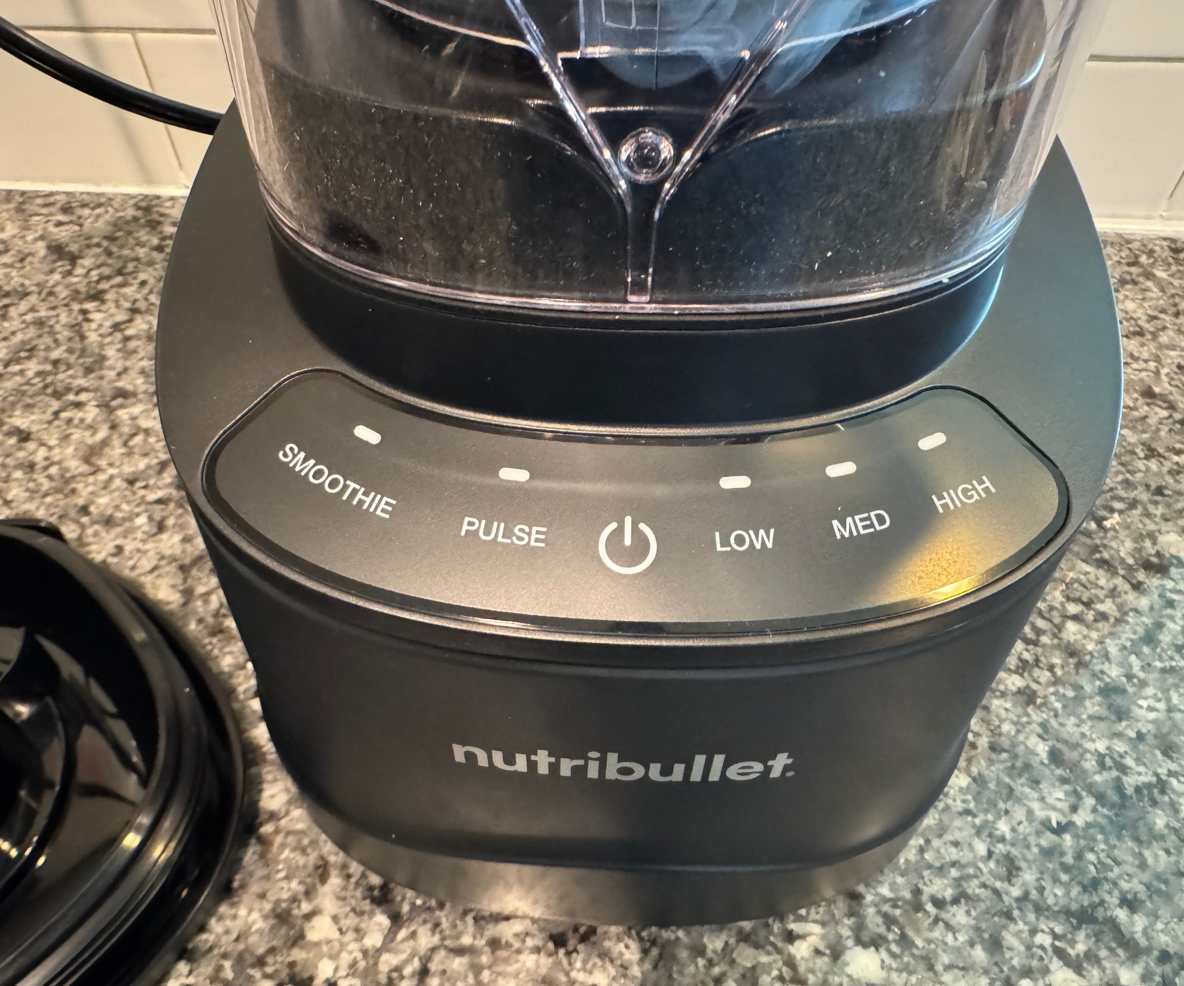 Eine Nahaufnahme der Basiseinheit eines Nutribullet PowerCore XL-Mixers auf einer Küchentheke aus Stein vor weißen U-Bahn-Fliesen.