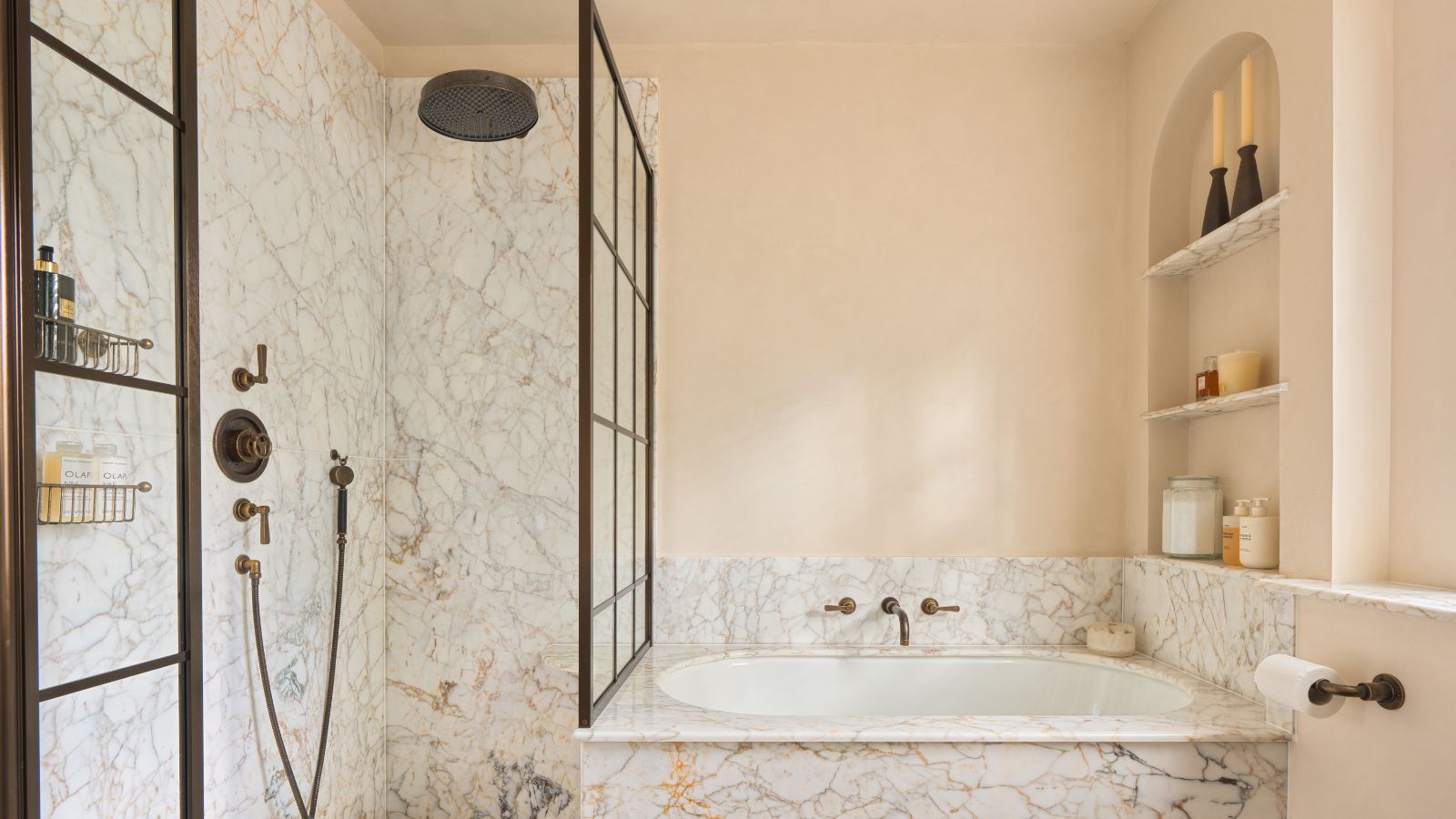 Ein kleines Badezimmer mit Marmorfliesen in Badewanne und Dusche, einer eingelassenen Wandnische mit Produkten und Glaskanistern sowie schwarzen Akzentdetails