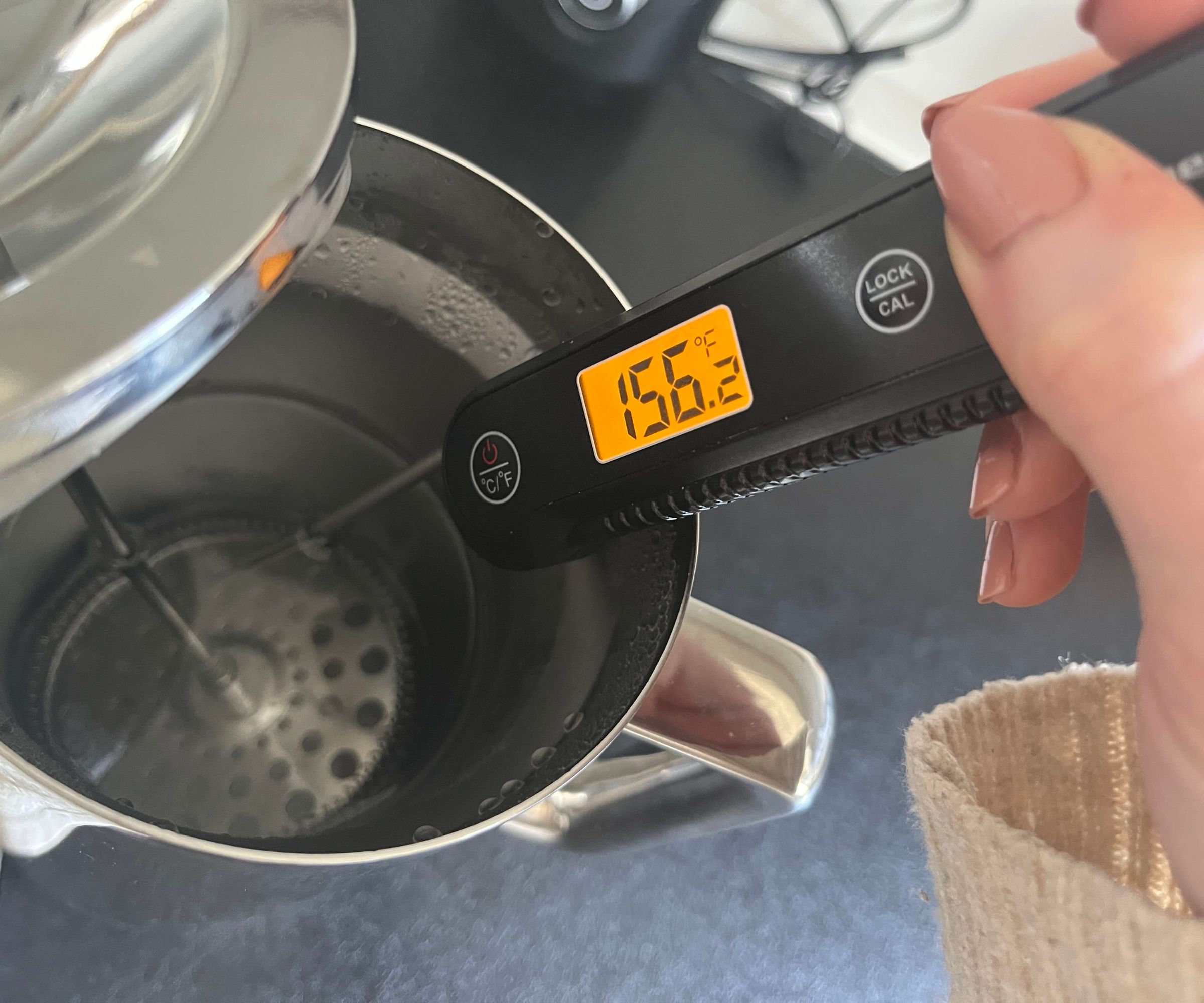 Ein digitales Thermometer, das die Wassertemperatur in einer Kaffeepresse aus Edelstahl misst. Es zeigt 156F