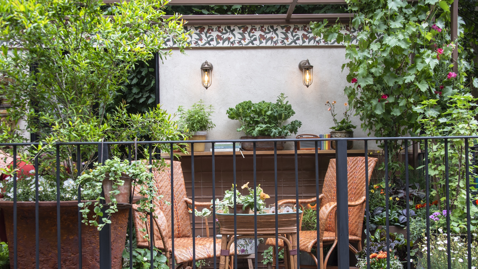 Balkongarten mit zwei braunen Korbstühlen im Vintage-Stil, umgeben von vielen Töpfen