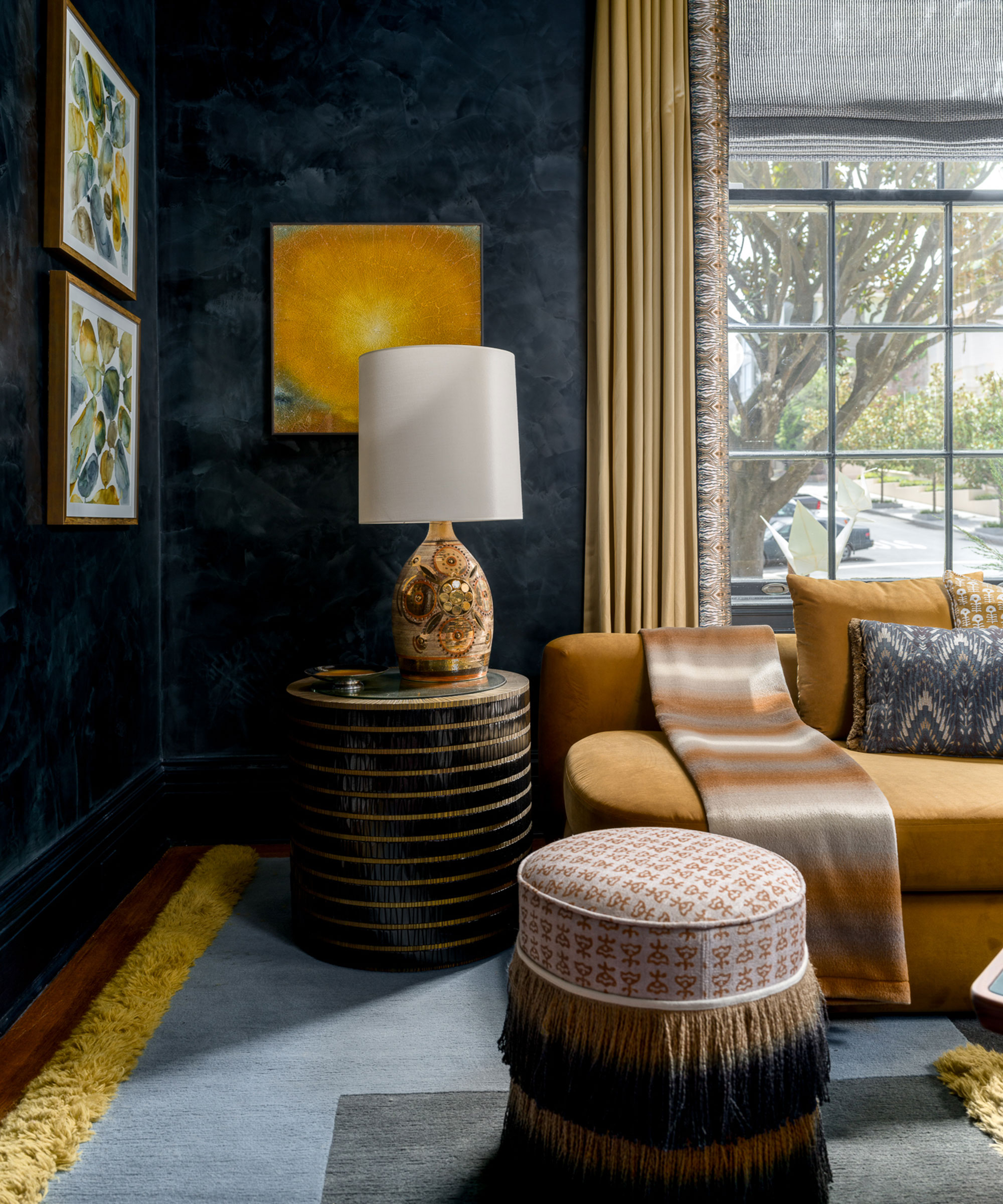 Eine elegante Wohnzimmerecke mit dunklen, strukturierten Wänden in Marineblau, kontrastiert von einem weichen senfgelben Sofa und goldenen Vorhängen.