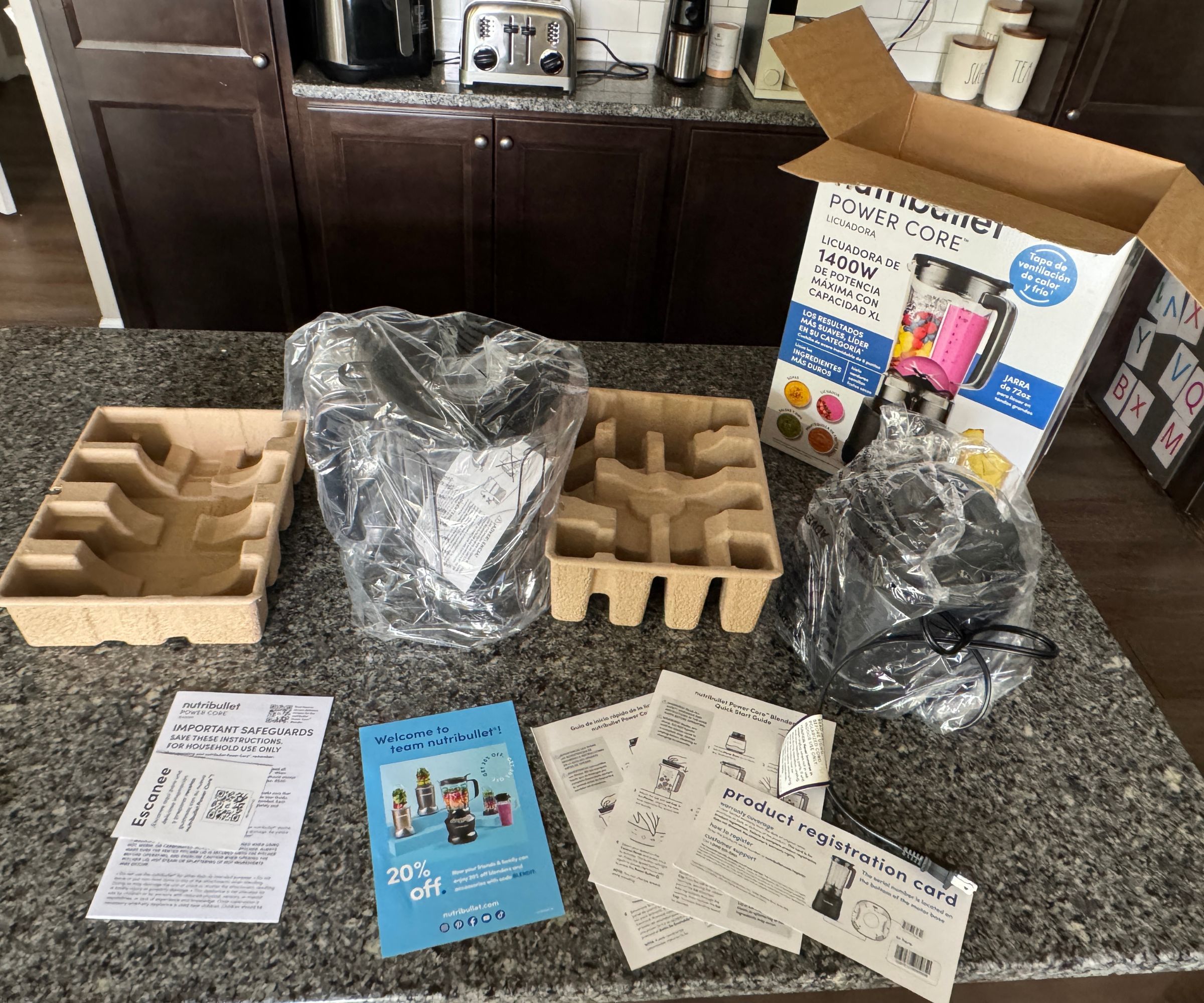 Alle Komponenten des Nutribullet PowerCore XL Mixers mit den Bedienungsanleitungen neben der Box auf einer Küchentheke aus Stein.