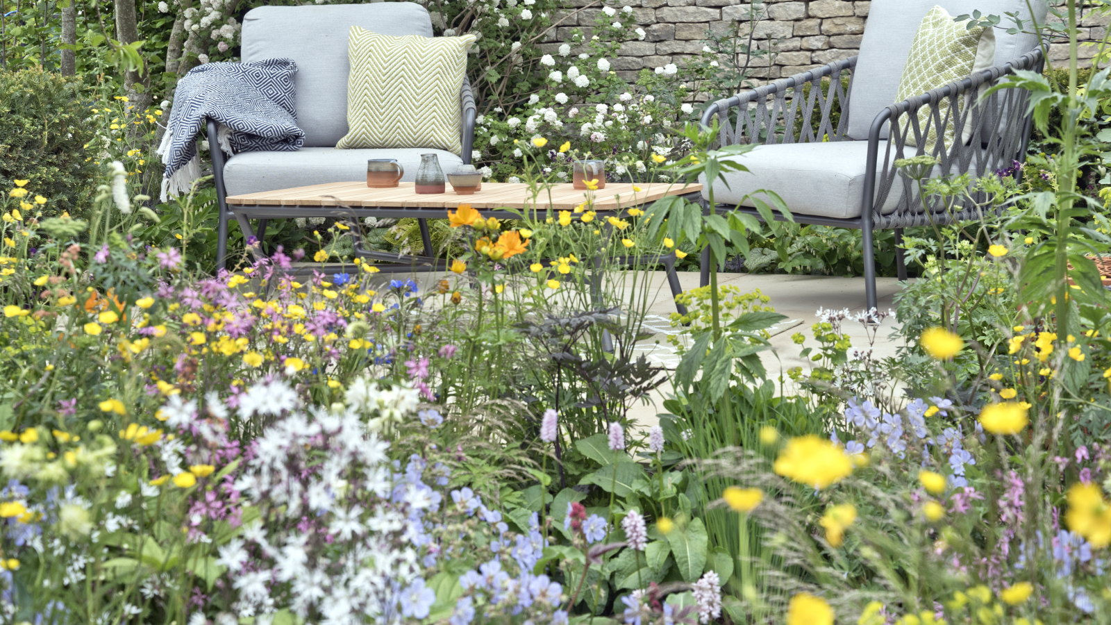 Ein farbenfrohes Blumenbeet vor einer entspannten gepflasterten Sitzecke