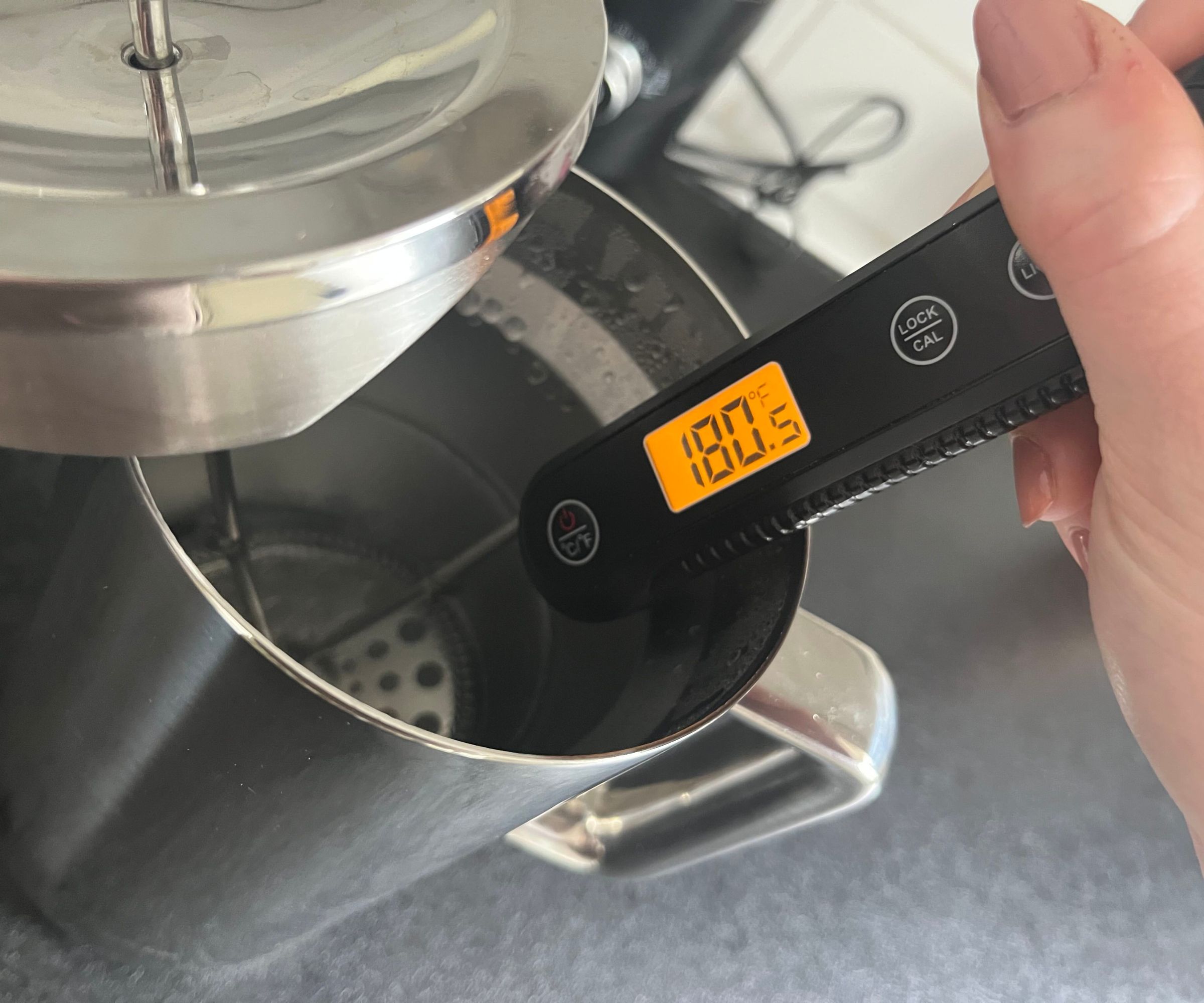 Ein digitales Thermometer, das die Wassertemperatur in einer Kaffeepresse aus Edelstahl misst. Es zeigt 180F