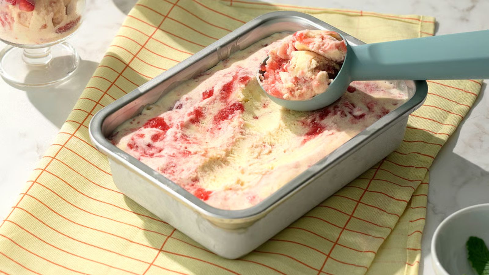 Ein kleiner rechteckiger Lebensmittelbehälter aus Edelstahl, gefüllt mit Eiscreme und einer Kugel oben drauf 
