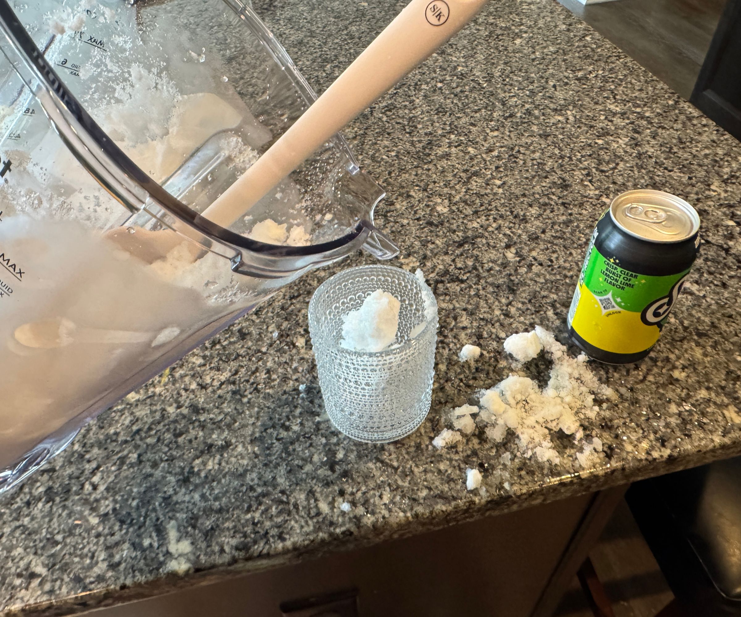 Eis wird aus einem durchsichtigen Mixerkrug in ein Glas gegossen und ergießt sich auf die Arbeitsfläche.