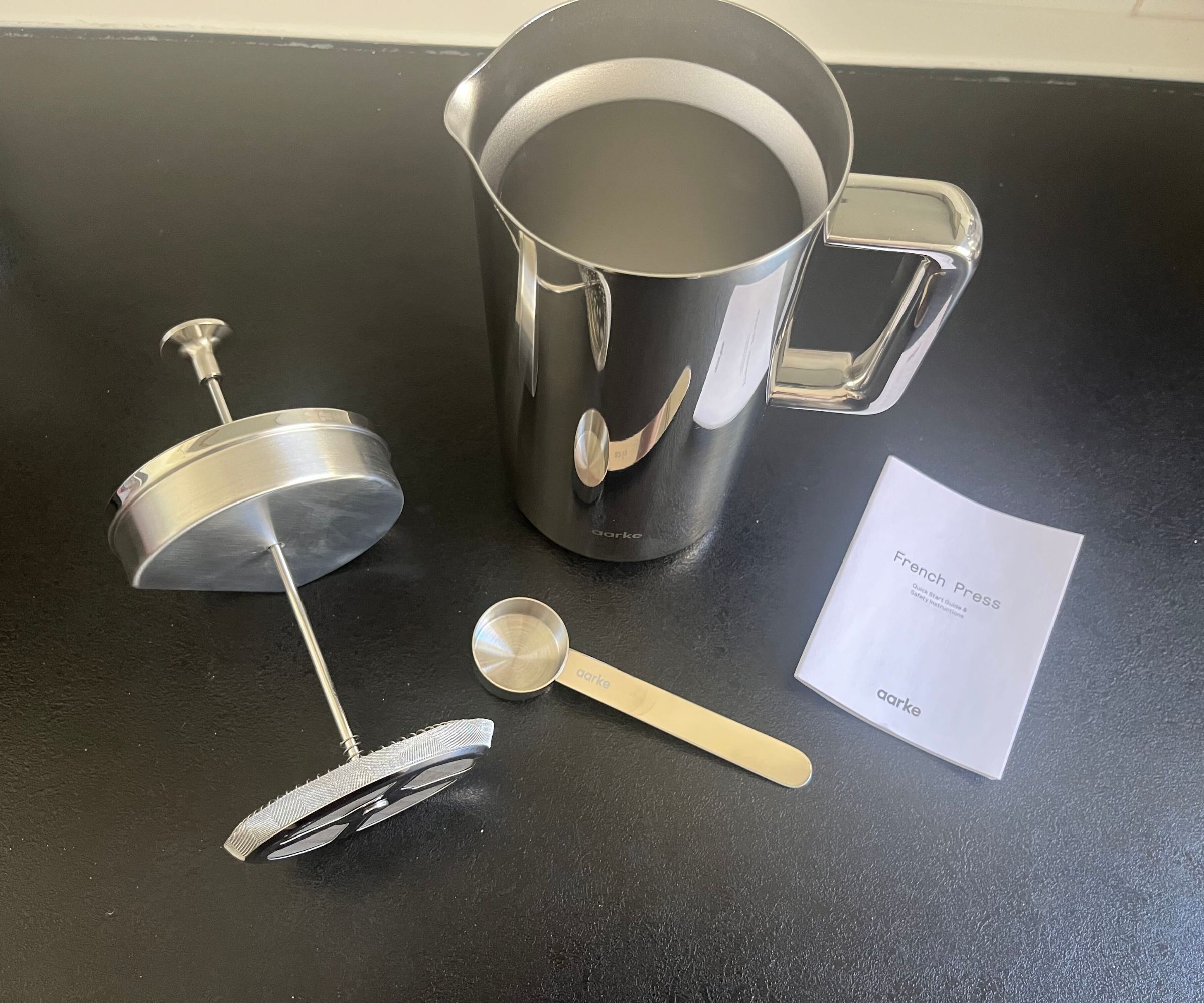 Eine Aarke-Kaffeepresse aus Edelstahl mit entferntem Kolben auf einer schwarzen Theke