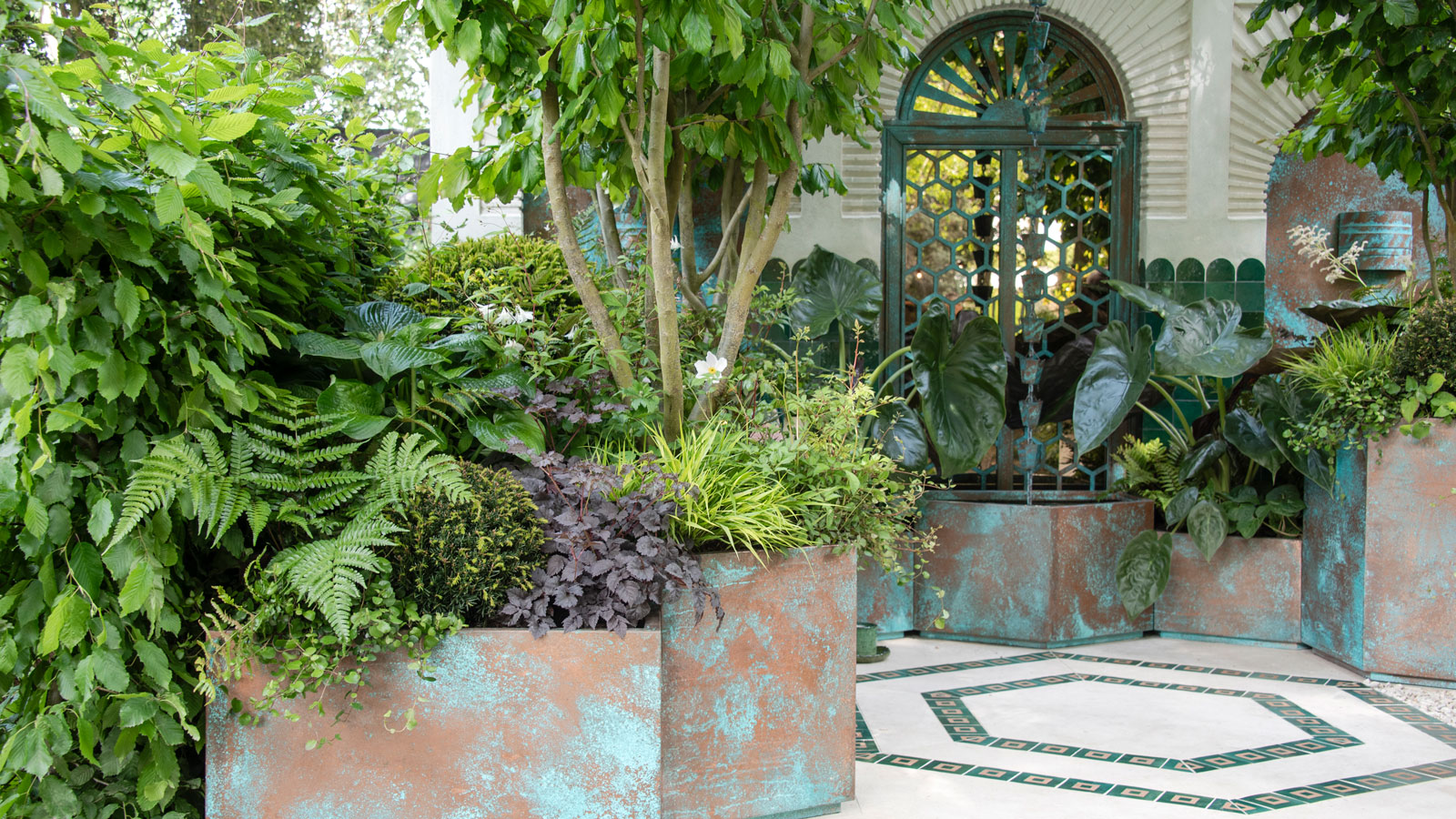 Innenhofgarten mit großen Pflanzgefäßen mit Bäumen und anderen Pflanzen sowie einem gepflasterten Terrassenbereich