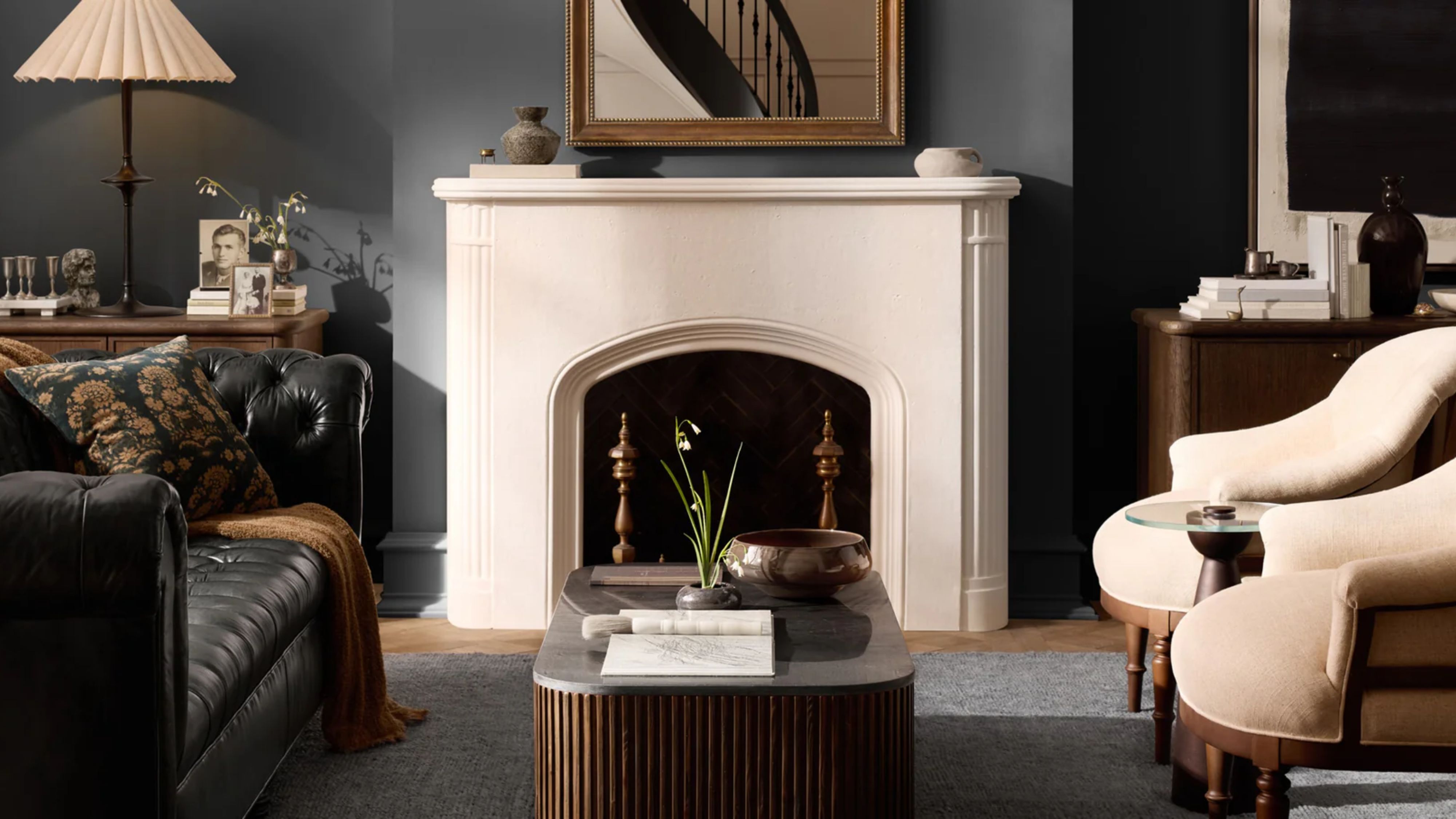 Stimmungsvolles Wohnzimmer mit einem schwarzen Chesterfield-Ledersofa, runden Sesseln, einem Couchtisch mit geriffelter Marmorplatte und gesammelten Gegenständen