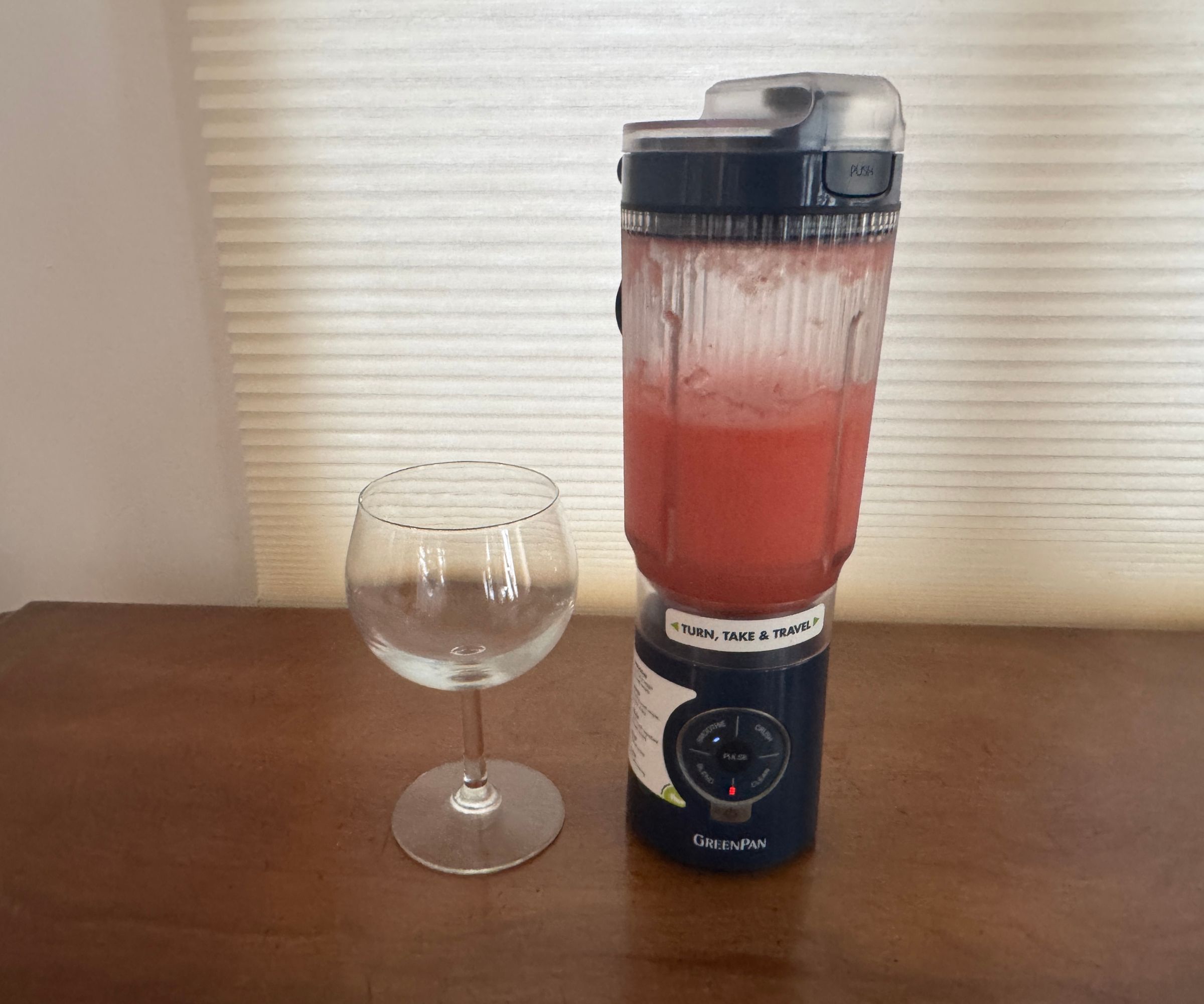 Eine rosa Flüssigkeit in einem schwarzen tragbaren Mixer neben einem Trinkglas.