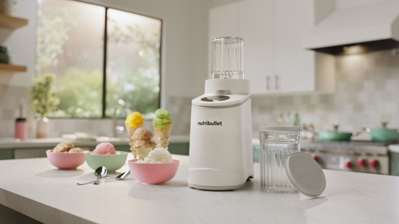 Eine weiße Nutribullet Chill-Eismaschine auf einer weißen Küchentheke, umgeben von kleinen Schüsseln mit Eis. 