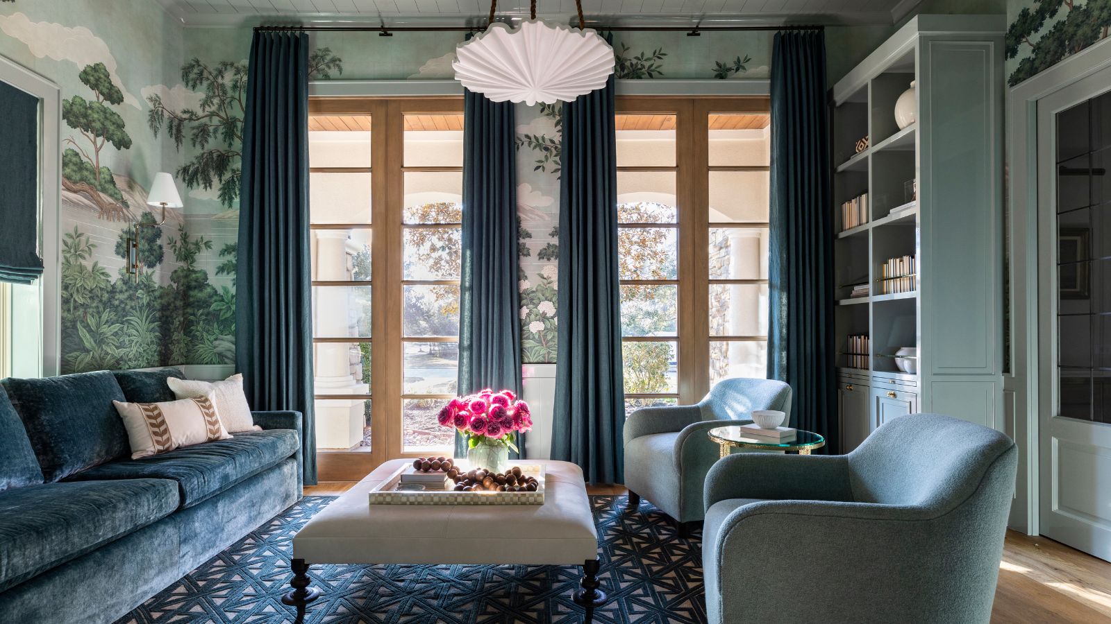 Traditionelles Wohnzimmer mit hellblauem Wandgemälde, blaugrünem Sofa und Sesseln, blauem Teppich und Vorhängen