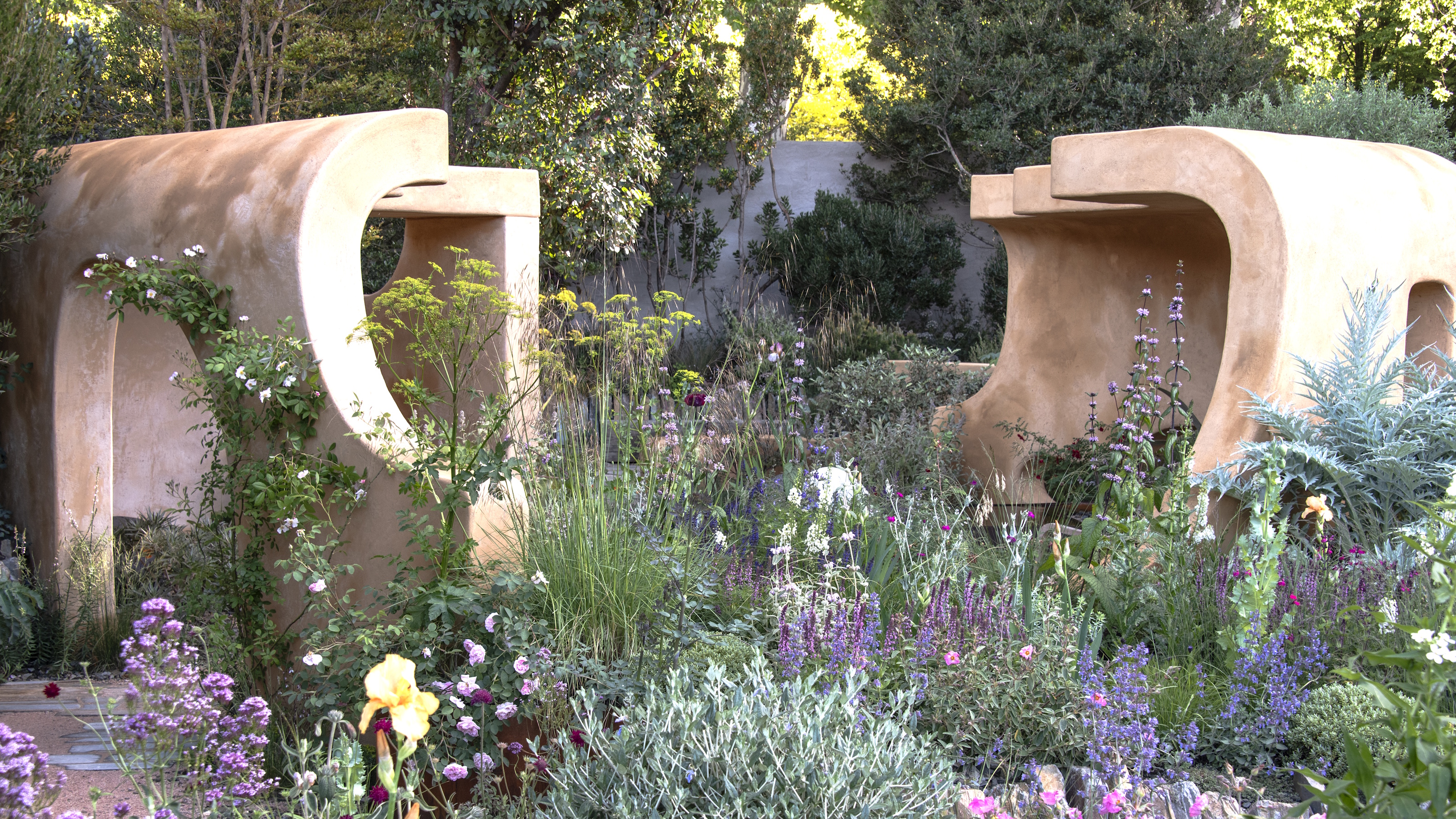 Ein großes, wildes Blumenbeet mit Salvia, Iris, Dill und einer Terrakotta-Struktur im Hintergrund