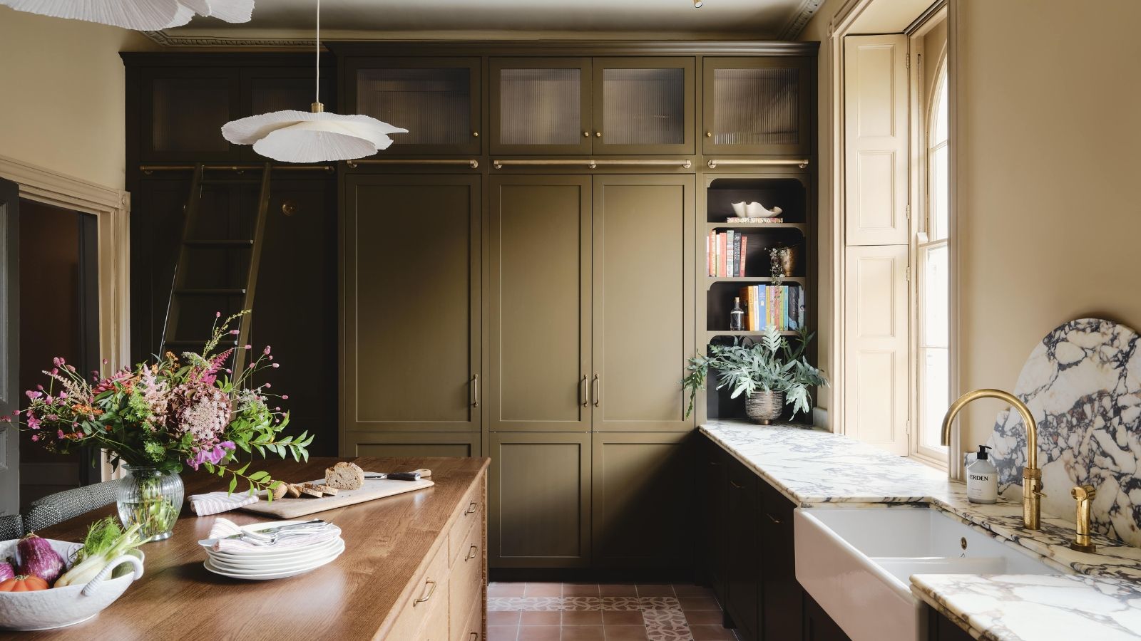 A kitchen with olive green cabinets, marble countertops, and a wooden island