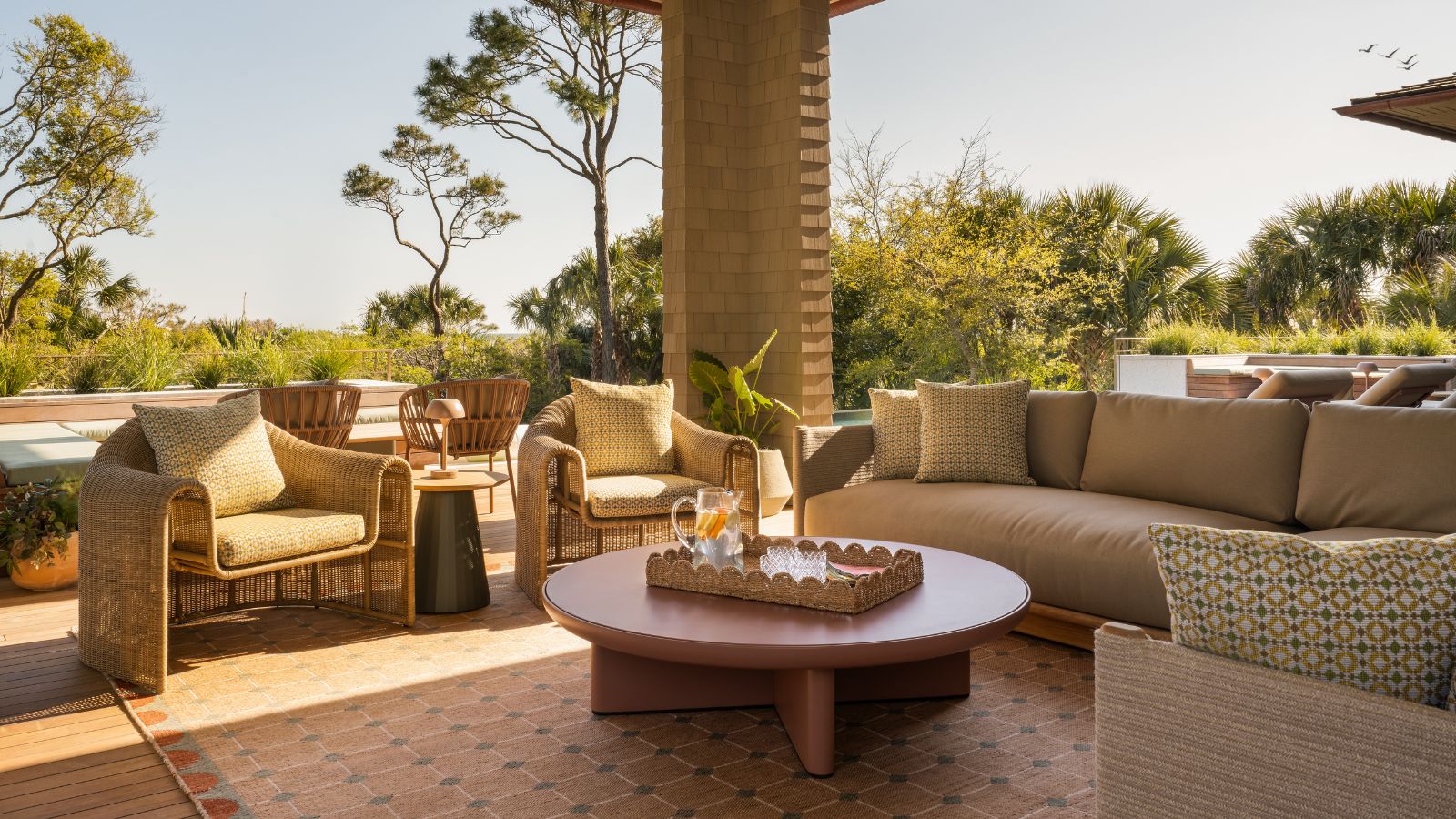 Wohnzimmer im Freien mit Korbstühlen, Sofa und Outdoor-Teppich in Erdtönen