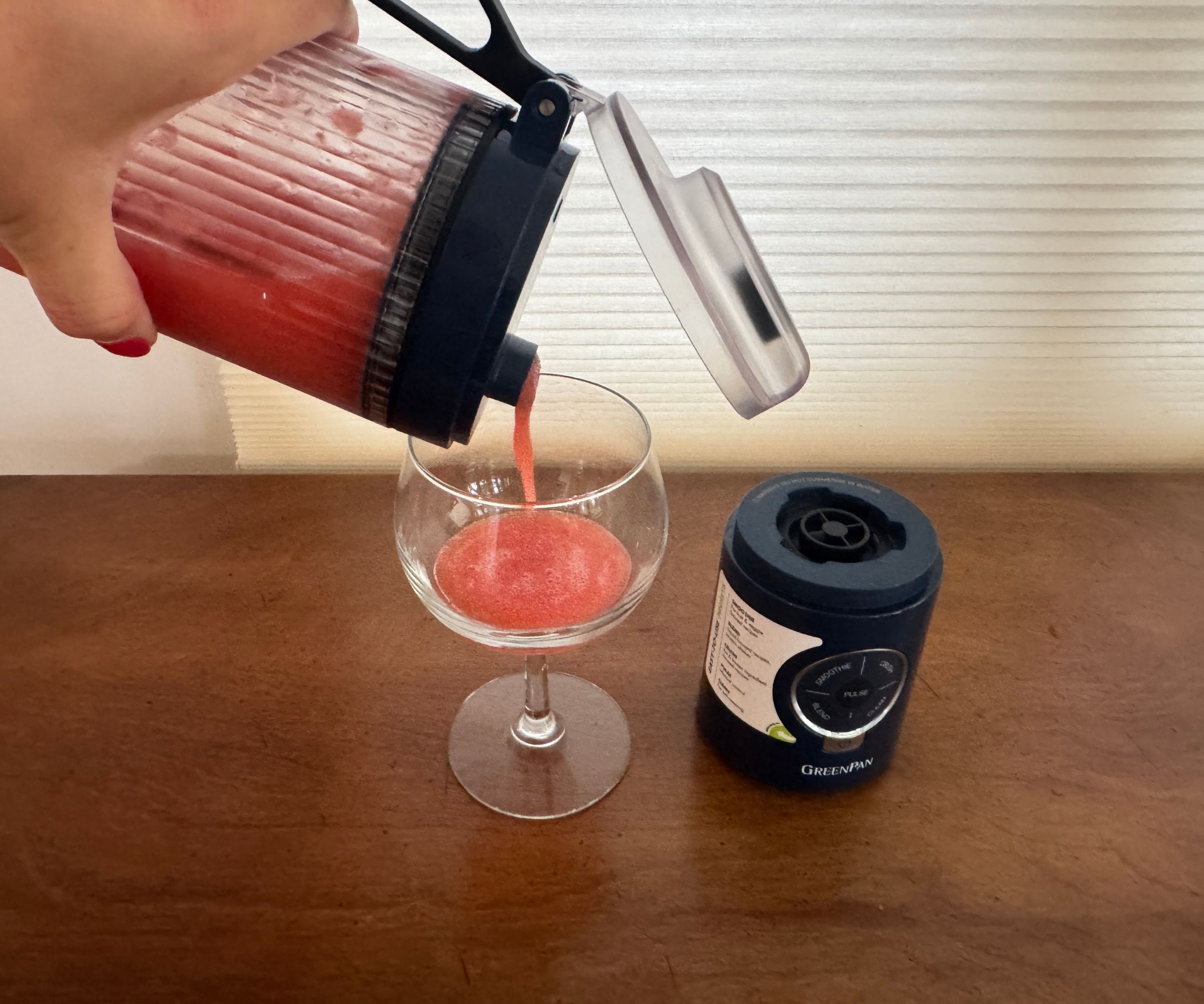 Eine rosafarbene Flüssigkeit aus einem schwarzen tragbaren Mixer in ein Trinkglas gießen.