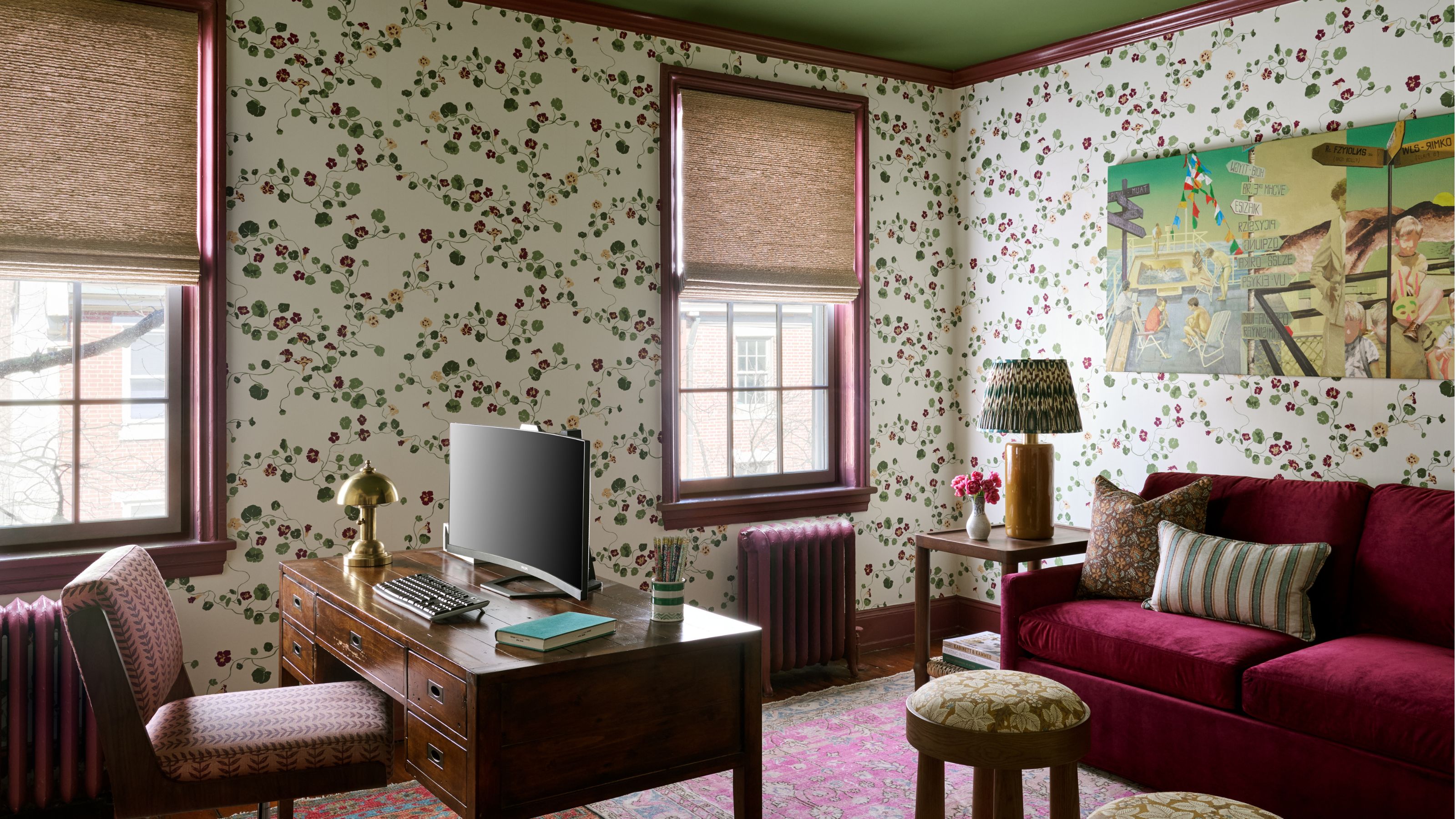 Heimbüro mit Blumentapete, grüner Decke, Vintage-Holzschreibtisch, burgunderfarbenem Samtsofa und einem leuchtend rosa Teppich.