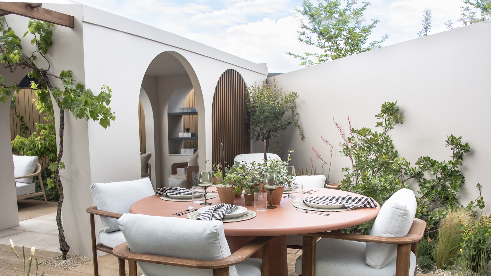 Ein runder Esstisch im Freien mit vier Stühlen auf einer modernen Terrasse mit weißen Wänden und Torbögen