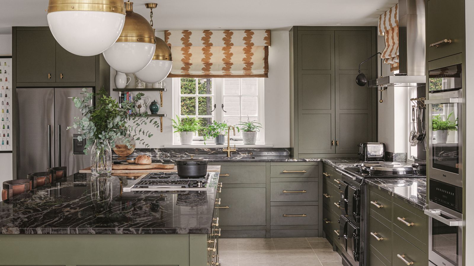 A large green painted kitchen with island. Black marble worktops.
