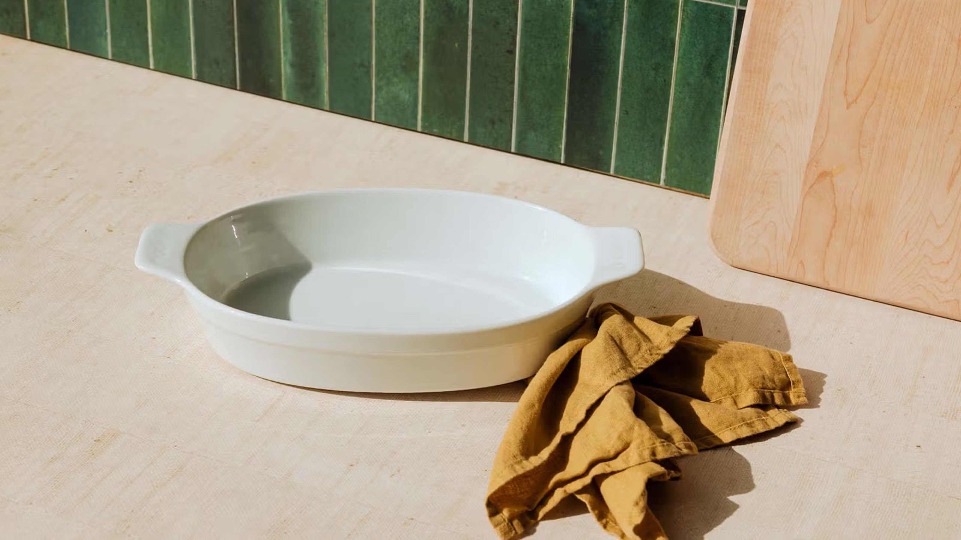 Eine ovale Backform aus weißem Porzellan auf einer Küchentheke aus Holz mit einer grünen Fliesenrückwand 