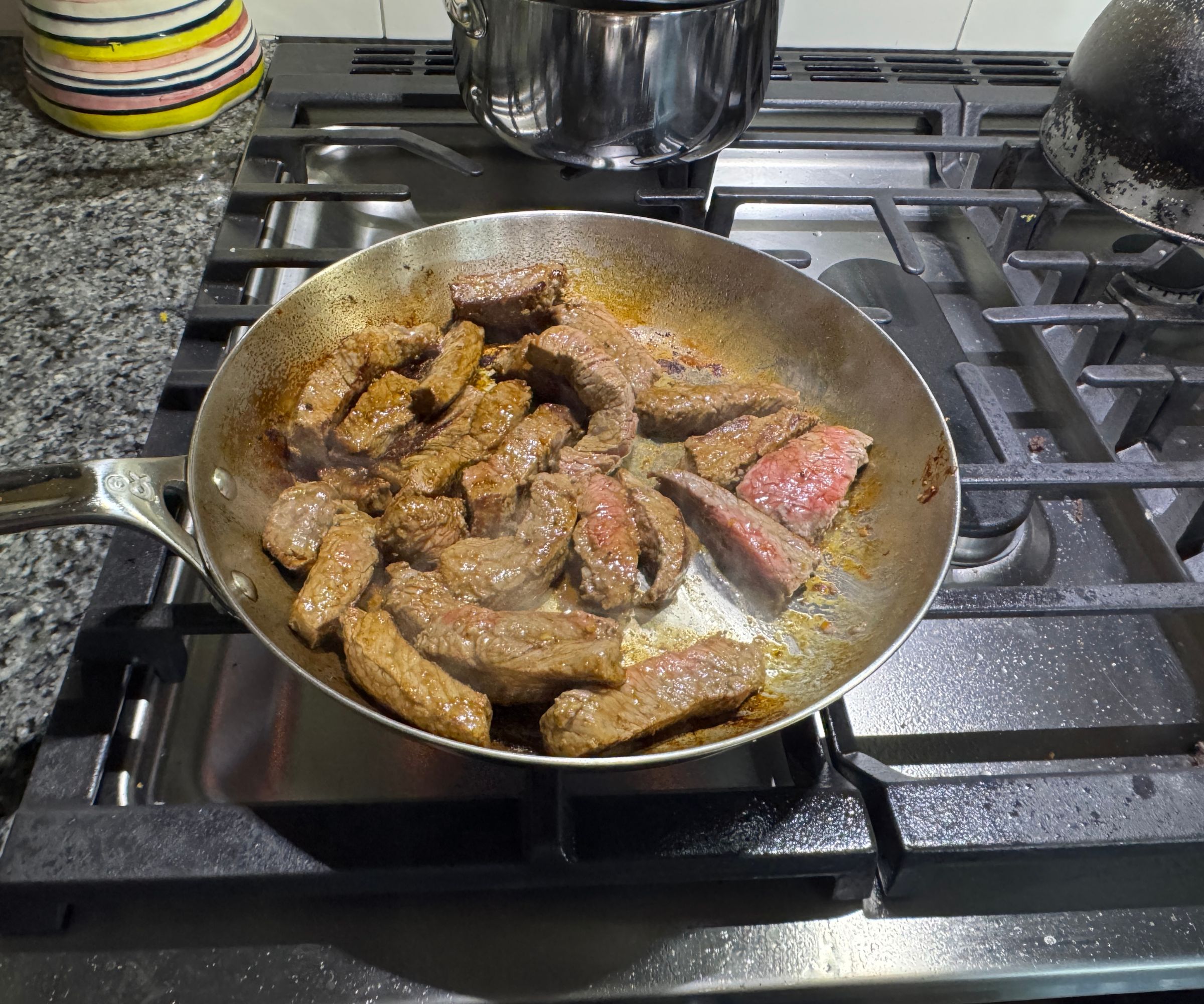 Eine kleine Bratpfanne aus Edelstahl auf einem Gasherd, gefüllt mit gebräunten Steakstreifen