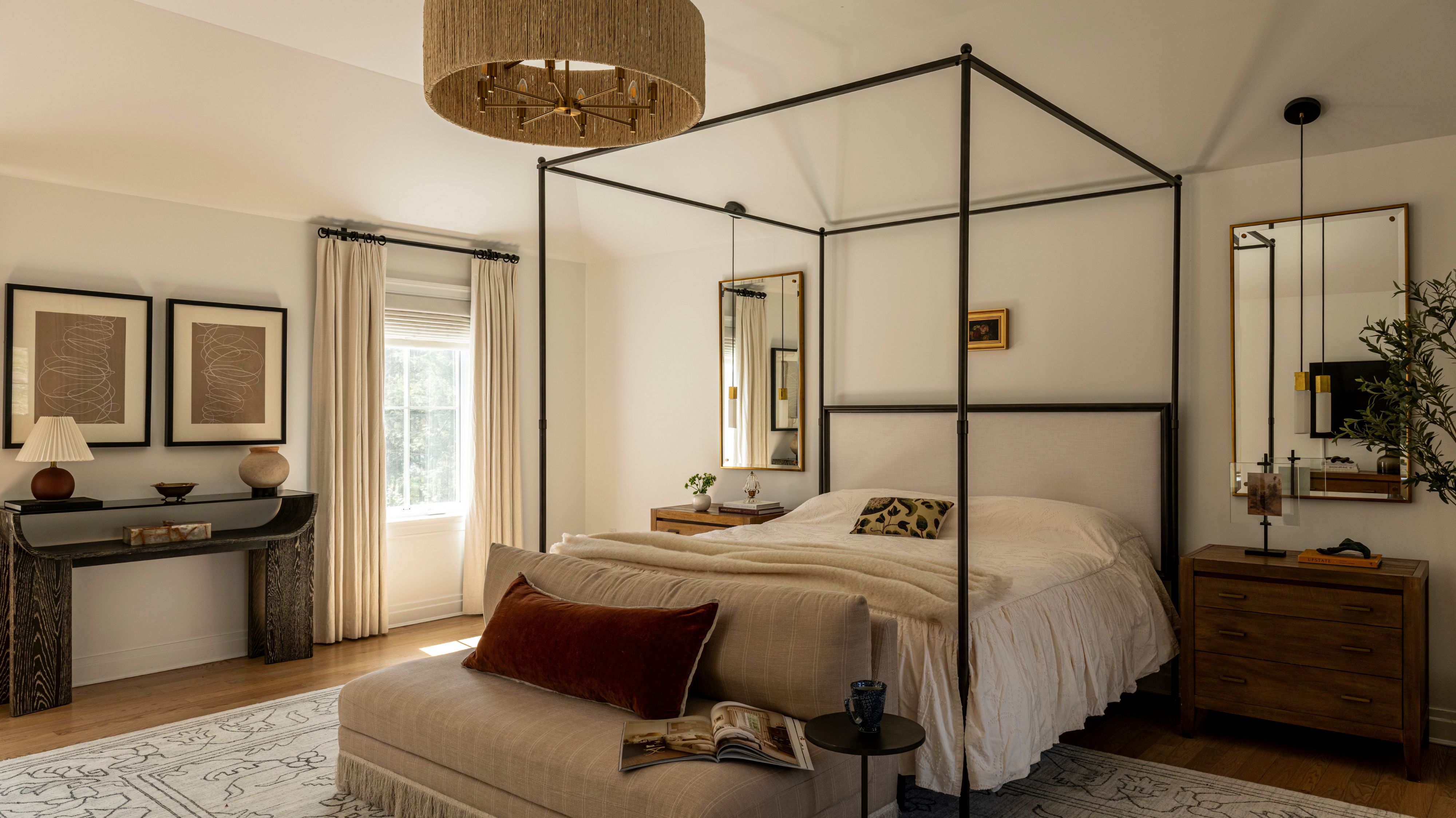 Luftiges Sommerschlafzimmer mit Himmelbett, gerüschtem Bettrock, gerahmter kleiner Kunst, neutralen Vorhängen und einem gewebten Kronleuchter an der Decke