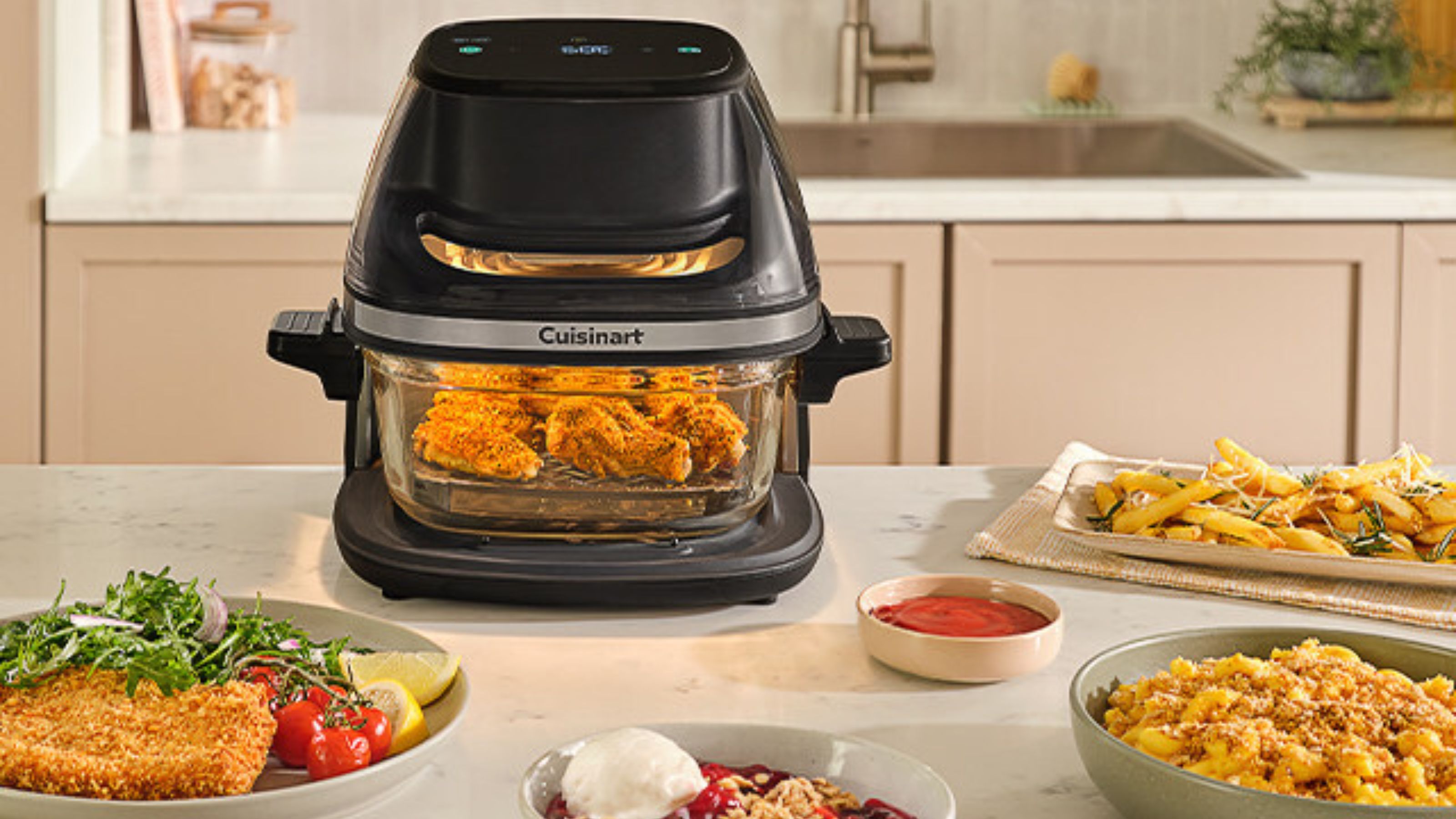 Die Cuisinart-Glasluftfritteuse auf einer weißen Arbeitsplatte, umgeben von gekochtem Essen. 