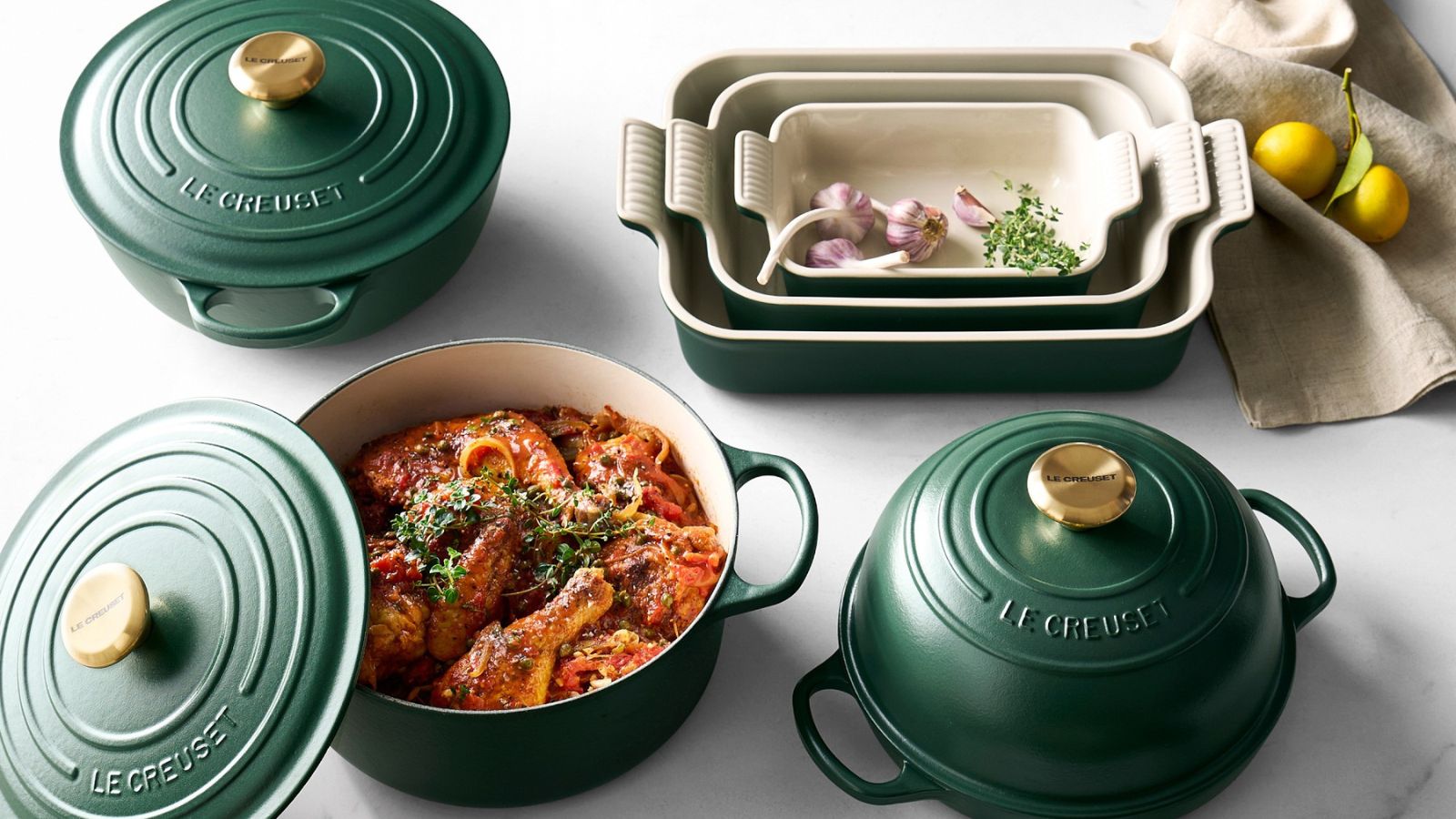 Die emaillierte Gusseisenkollektion von Le Creuset in tiefem Forêt-Grün auf einer Marmorplatte. 