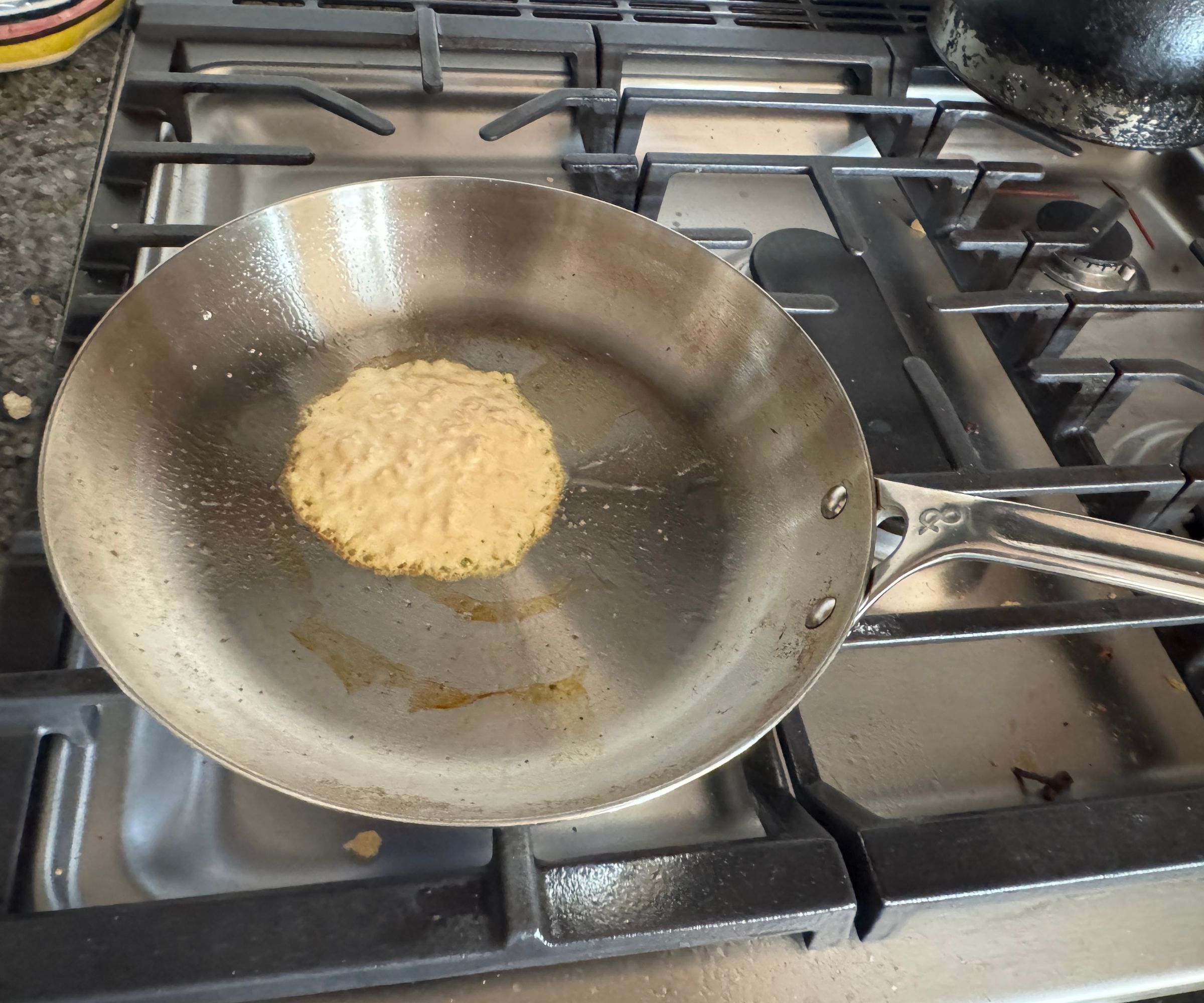 Eine Bratpfanne aus Edelstahl, in der ein einzelner Pfannkuchen auf einem Gasherd gebraten wird