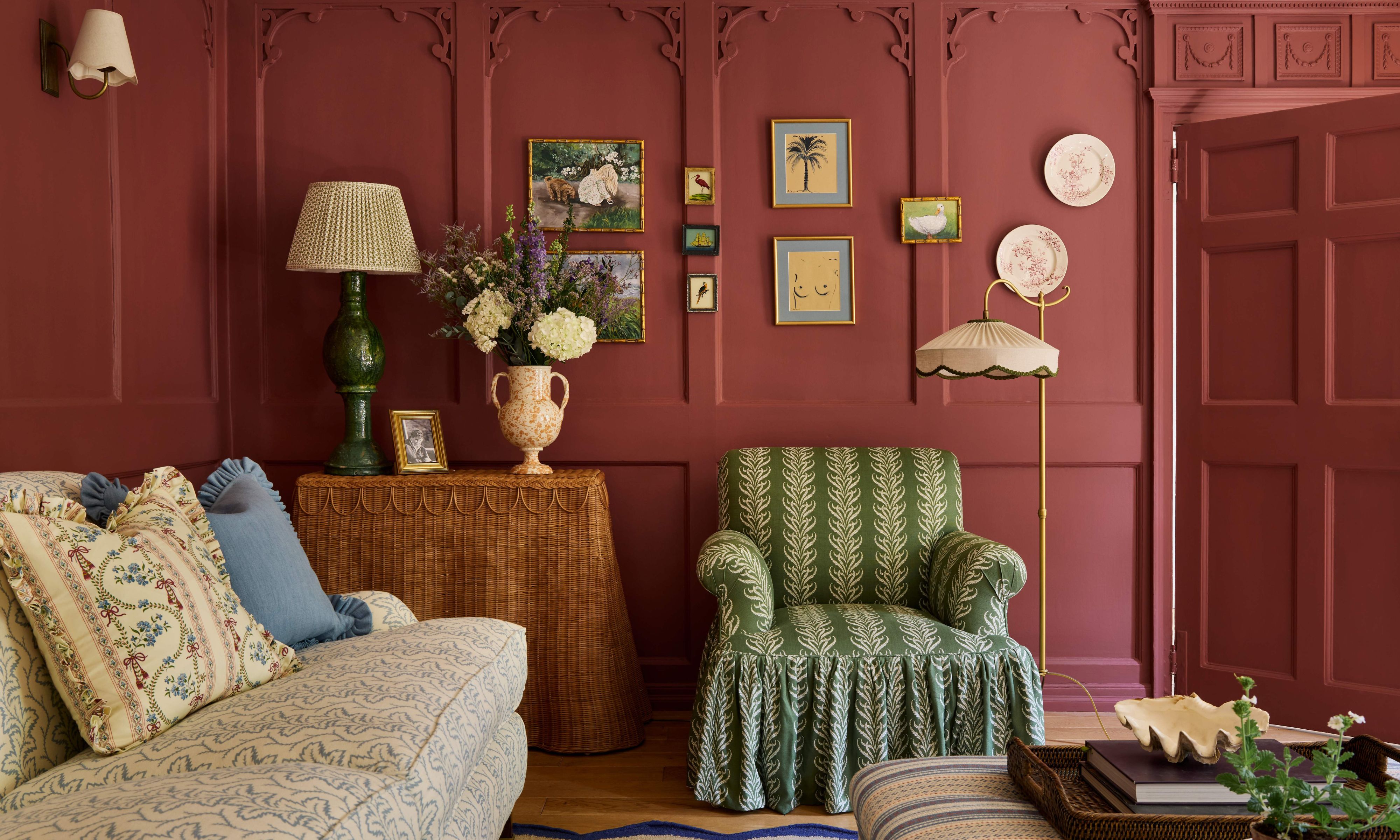 ein rot-rosa gestrichener Salon mit historischen Wandtäfelungen und Zierleisten, Möbeln mit Schürzen, winziger Kunst und einem gemusterten Sofa