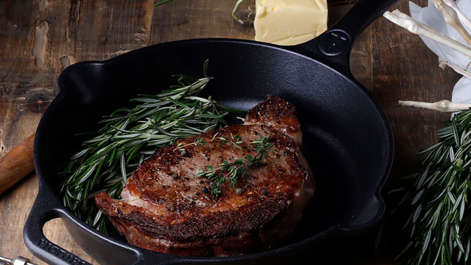 Eine schwarze Gusseisenpfanne auf einer Holzarbeitsplatte mit einem gebratenen Steak darin. 