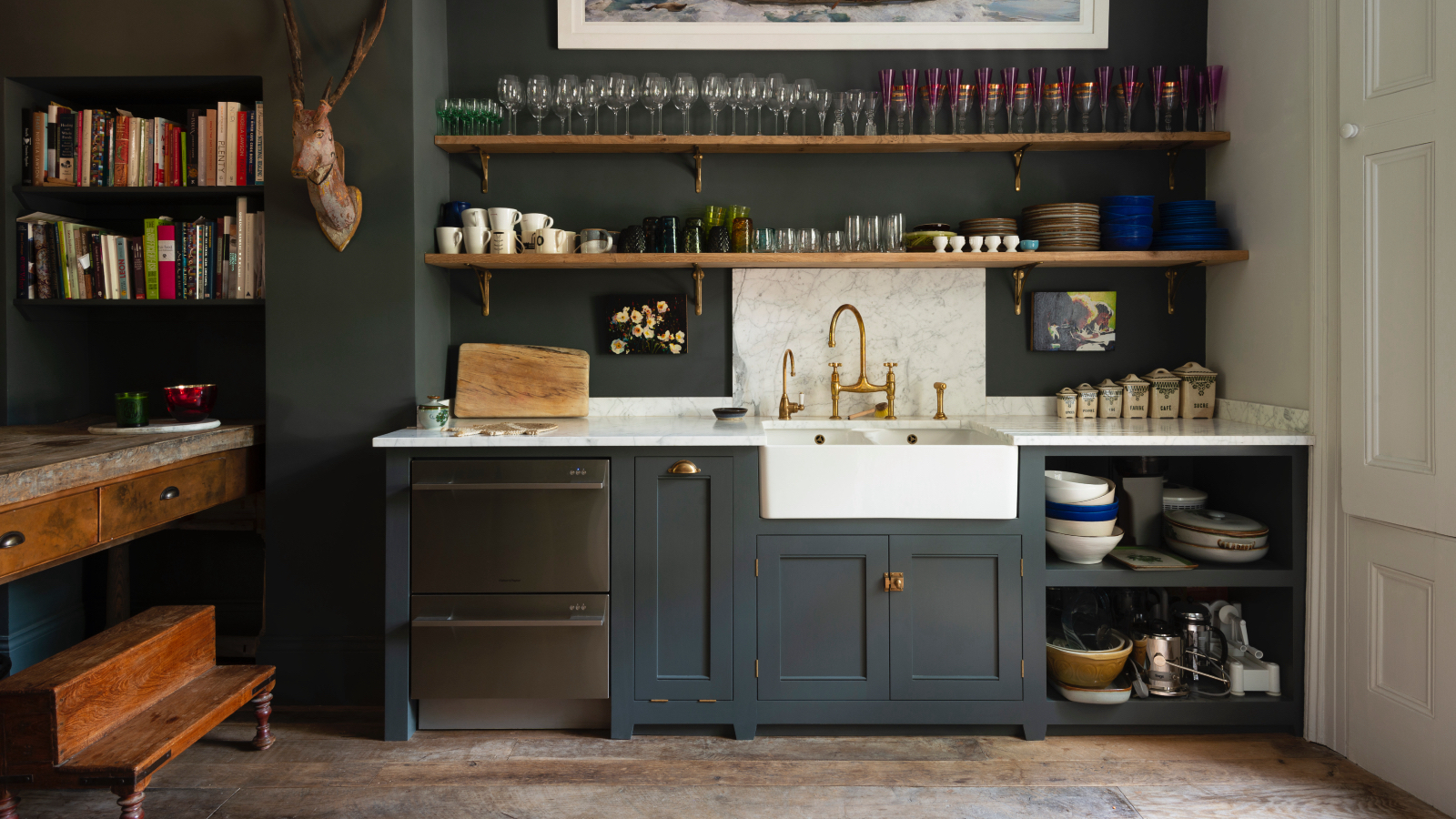 Offene dunkelblaue Küche, offene Regale mit Glaswaren, Rückwand und Arbeitsplatte aus Marmor, weißes Butler-Waschbecken, Holzdielen, deVOL