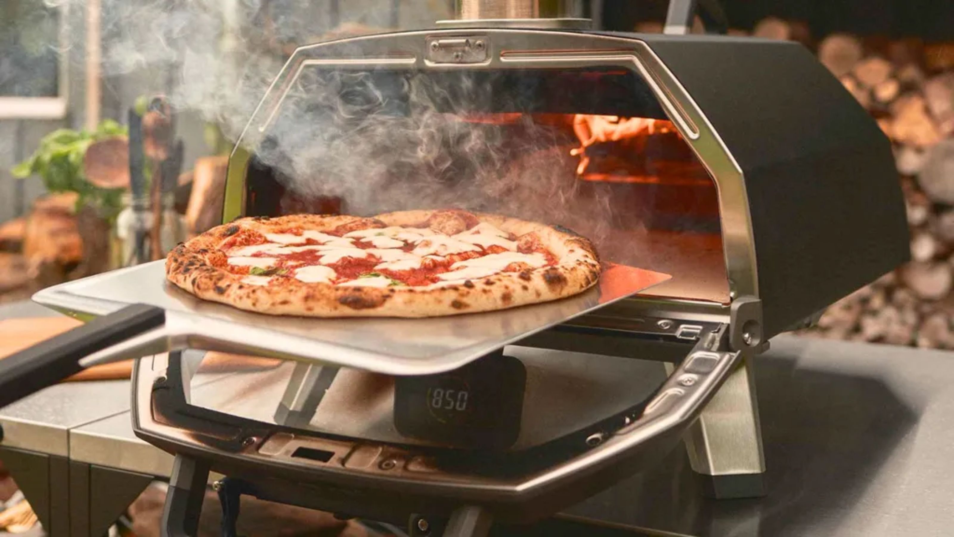 Ooni Karu 2 Pro mit einer frischen Pizza, die auf einem Pizzaschieber aus Metall herausgenommen wird. 