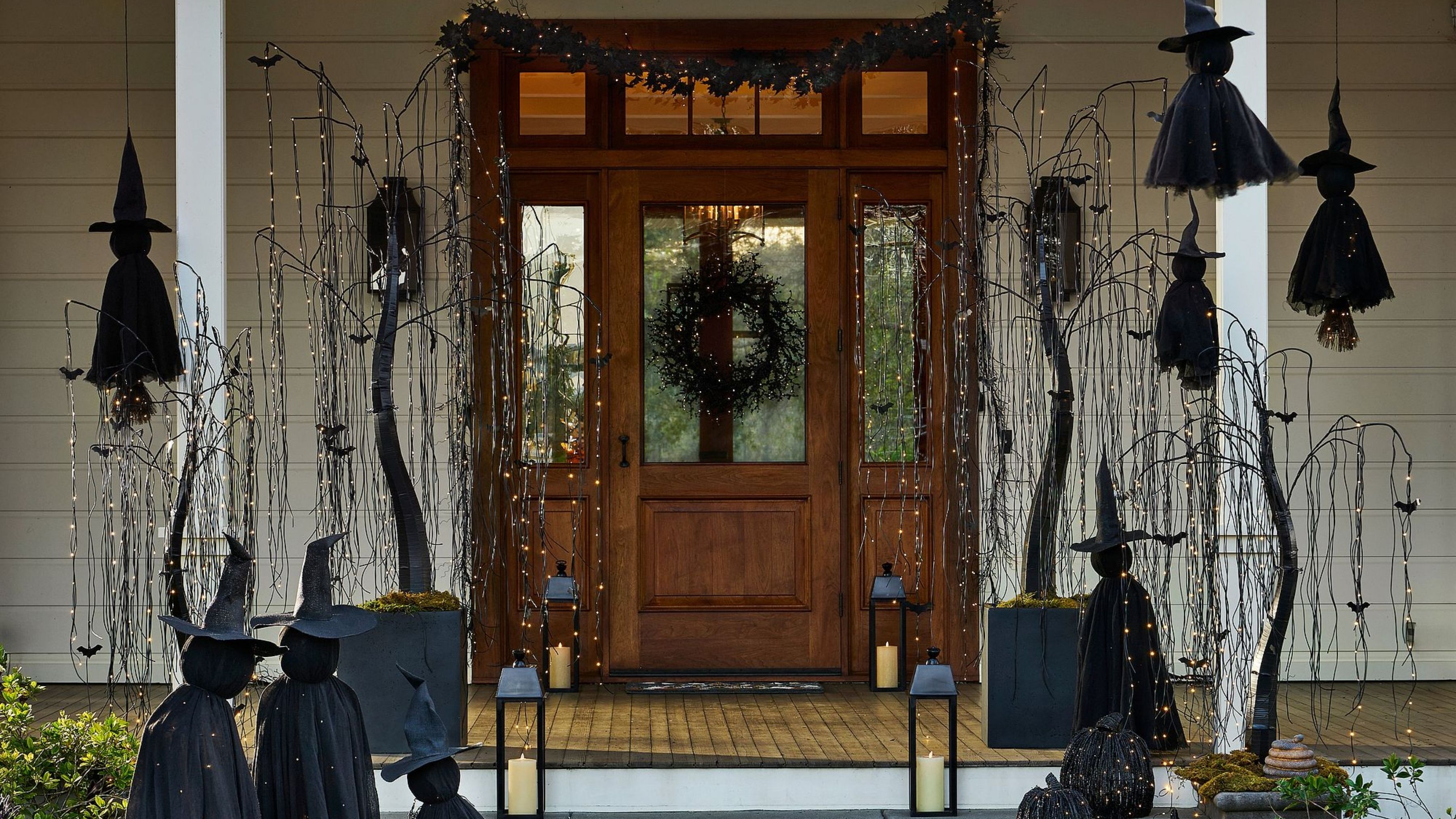Der vordere Verandabereich ist mit gotischen Halloween-Lichtern geschmückt, darunter funkelnde Weidenbäume, Hexen, Laternen und ein komplett schwarzer Kranz.