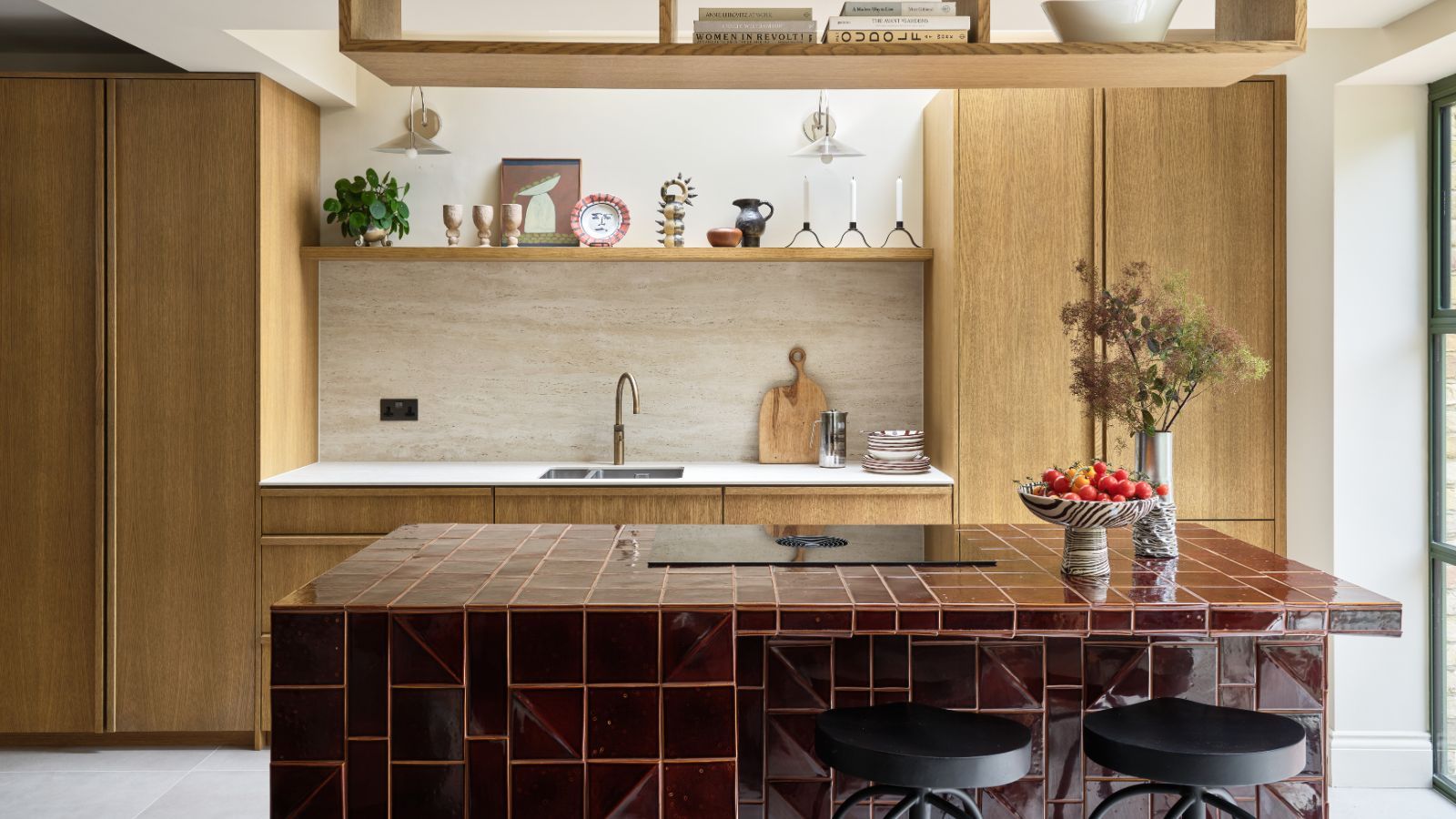 A modern kitchen with light wooden cabinets, and a red tiled island.