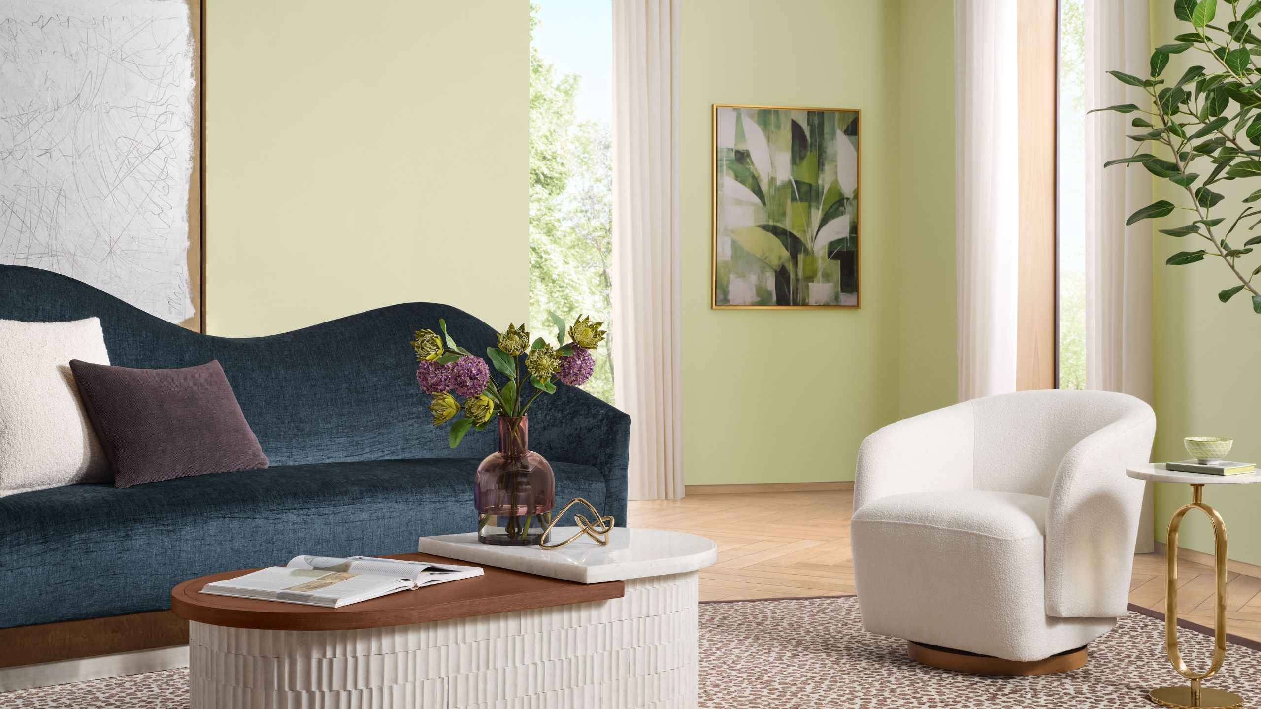 Wohnzimmer in Sherwin-Williams Celery gestrichen, mit Holzböden, einem cremefarbenen Bouclé-Sessel, einem marineblauen, geschwungenen Samtsofa, einem niedrigen Couchtisch aus Holz und einem großen Olivenbaum in der Ecke.
