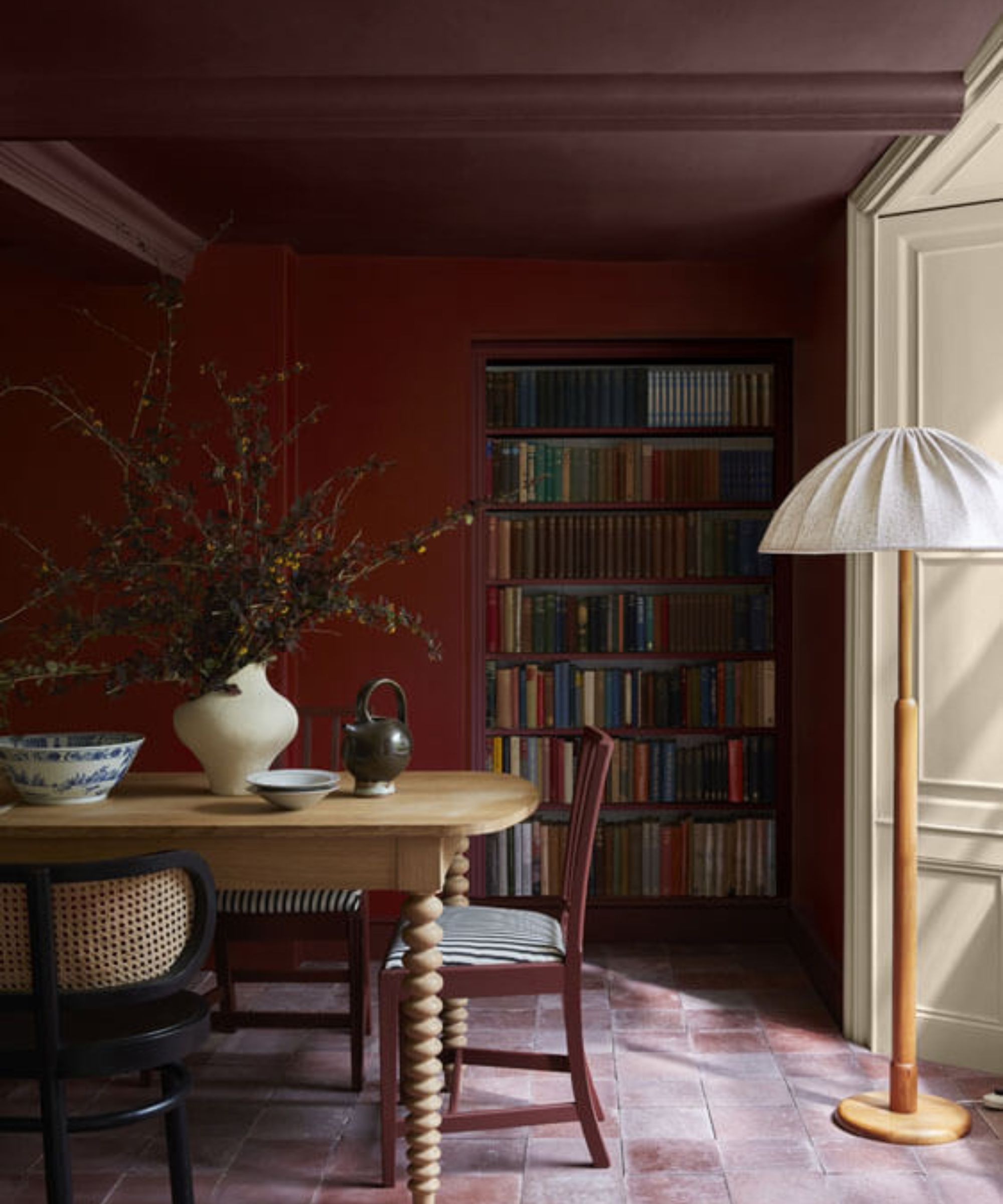 Ein farbenfrohes, rotes Esszimmer mit einem Esstisch aus Holz, dekoriert mit einer Vase mit Herbstlaub und einer Holzlampe mit weißem Schirm