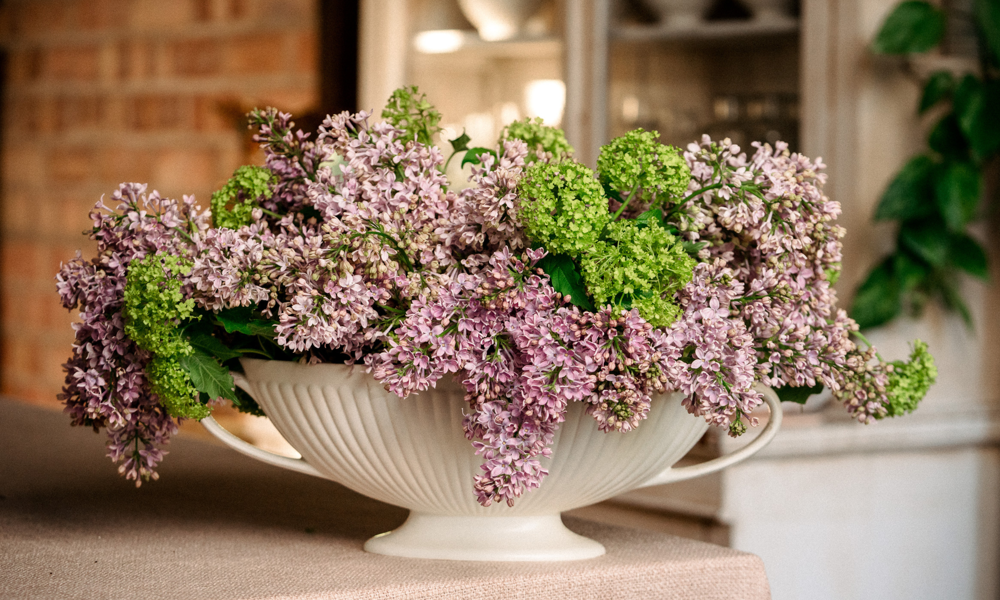 Blumenmuster aus lila und grünem Viburnum opulus in einer weißen Keramik-Bootsvase