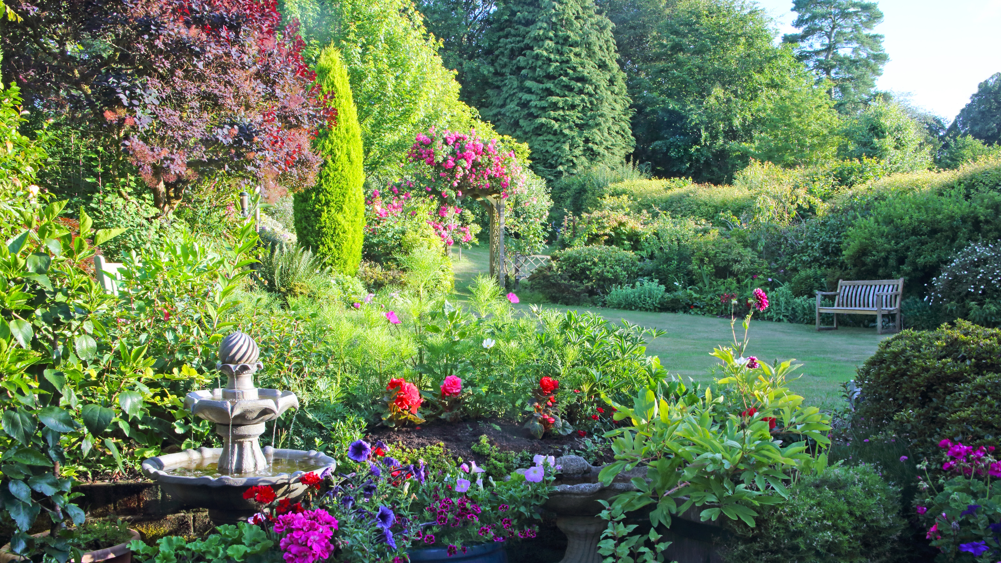 Englischer Garten voller bunter Blumen und steinernes Vogelbad im Sommer