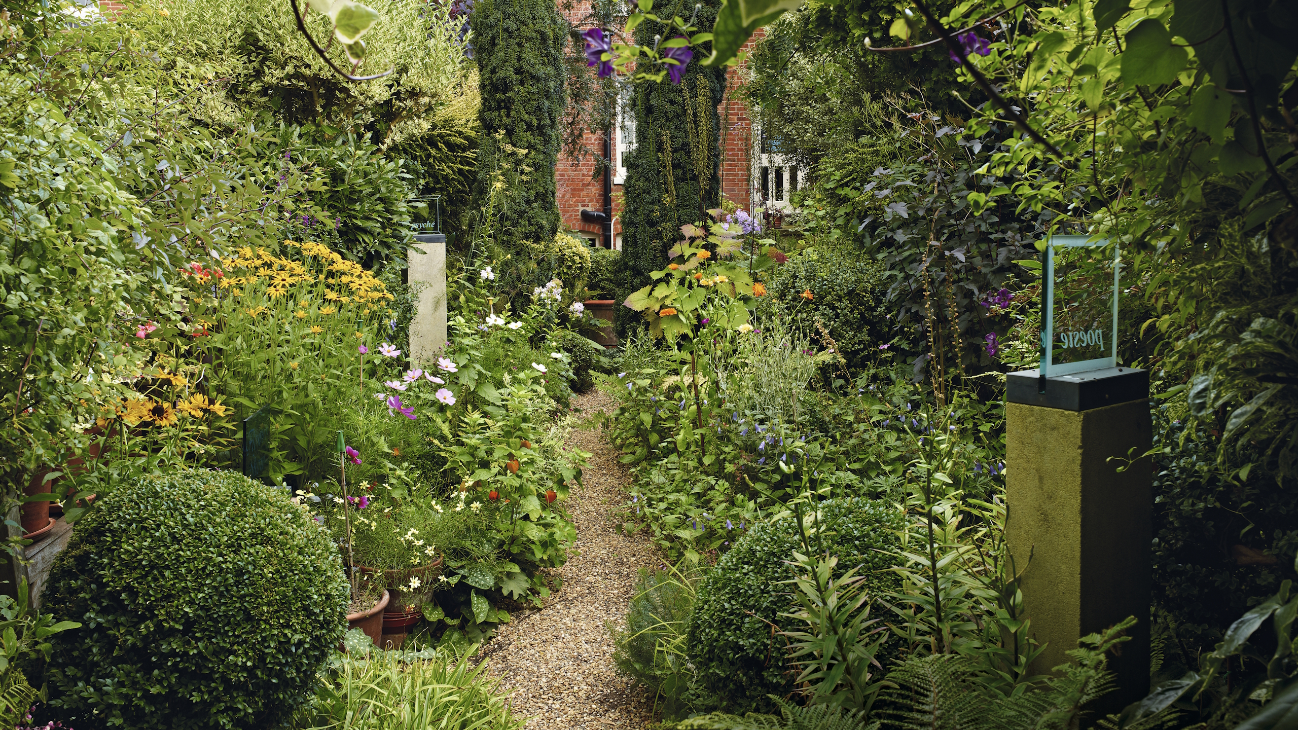 Zu beiden Seiten eines Kieswegs grenzt ein Stadtgarten voller Blumen