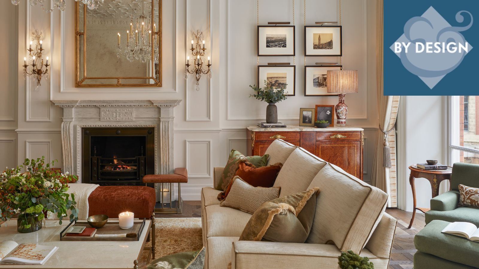 Luxurious living room with white panelled walls, artwork and wall lamps, cream sofa and coffee table in fron of fireplace, windows and green seating to the right