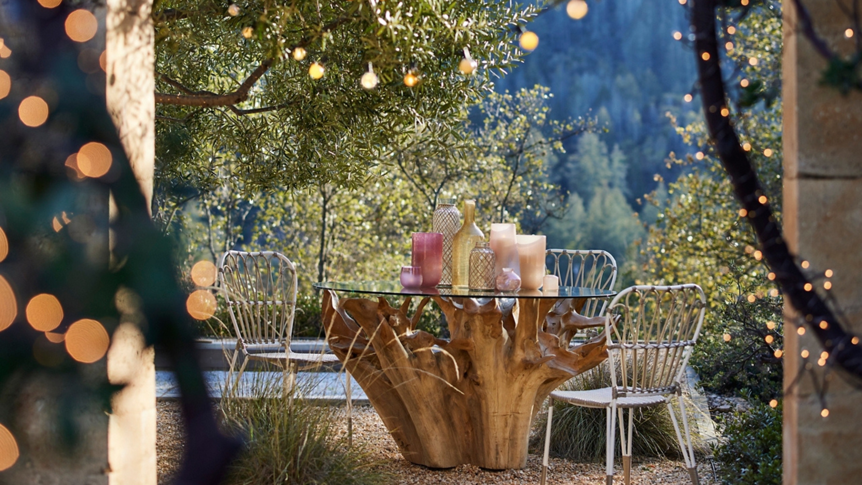 eine Terrasse mit Holztisch und Metallstühlen und herumhängenden Lichterketten