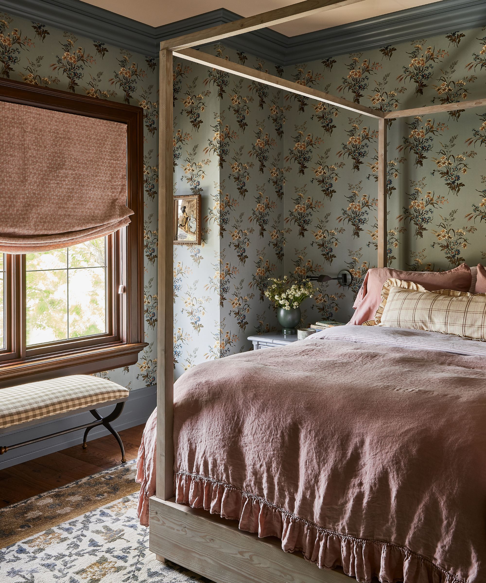 Bunt gemustertes Schlafzimmer mit blauer Blumentapete, rosafarbenem Rollo, rosafarbener Bettwäsche und hölzernem Himmelbett