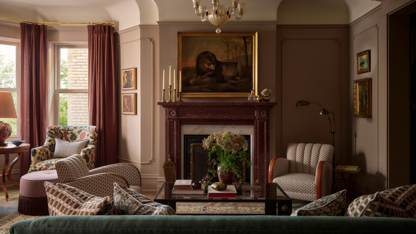 Wohnzimmer mit grünem Samtsofa, gemusterten Sesseln, rosa Vorhängen, Marmorkamin, antiken Kunstwerken und geschichteter Beleuchtung.