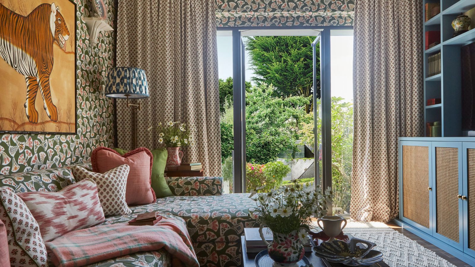 Ein gemustertes Wohnzimmer in London von der Designerin Elizabeth Hay mit Terrassentüren zum Garten und einer blauen Medienwand