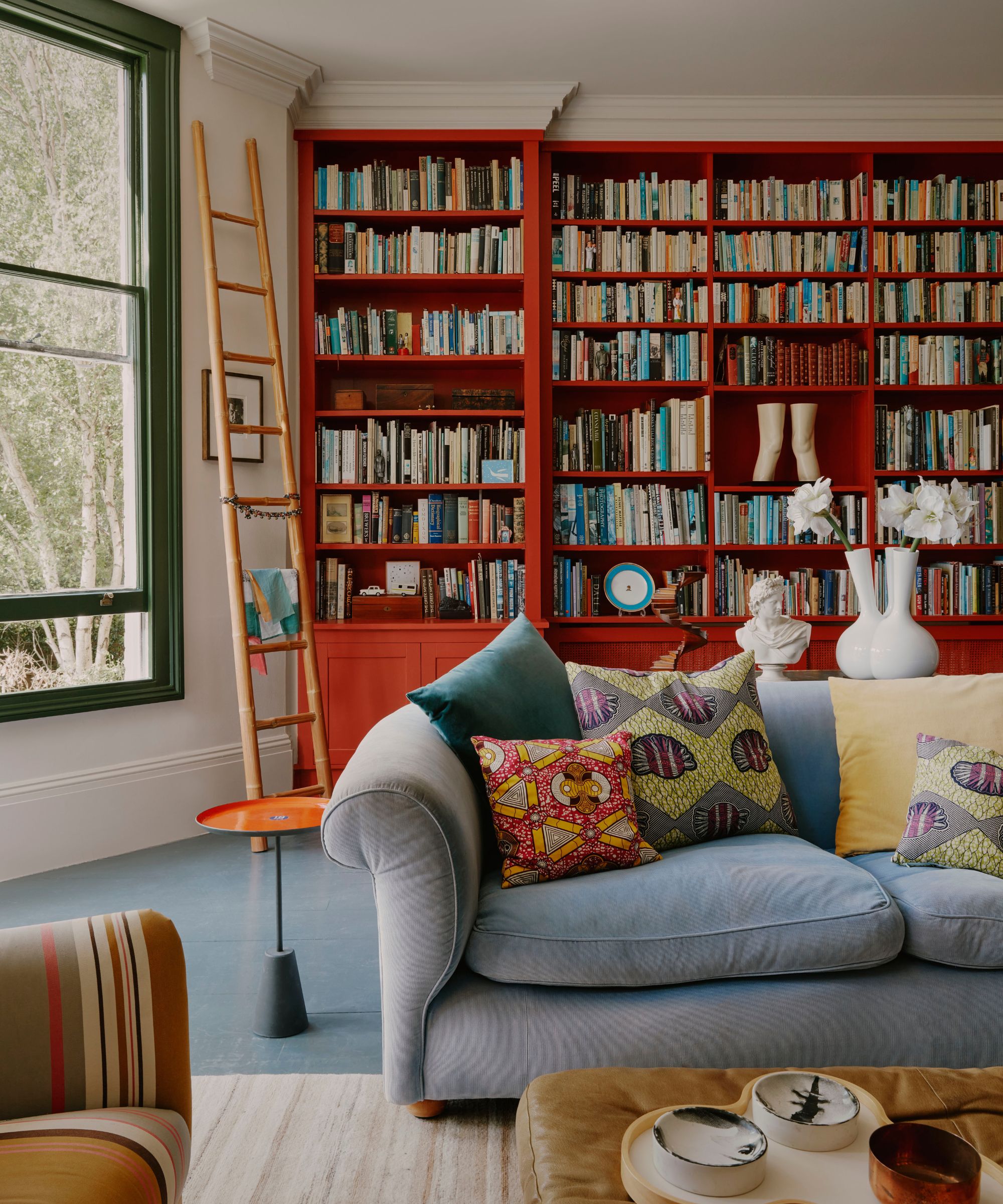 Wohnzimmer mit raumhohem roten Bücherregal und grauer Couch