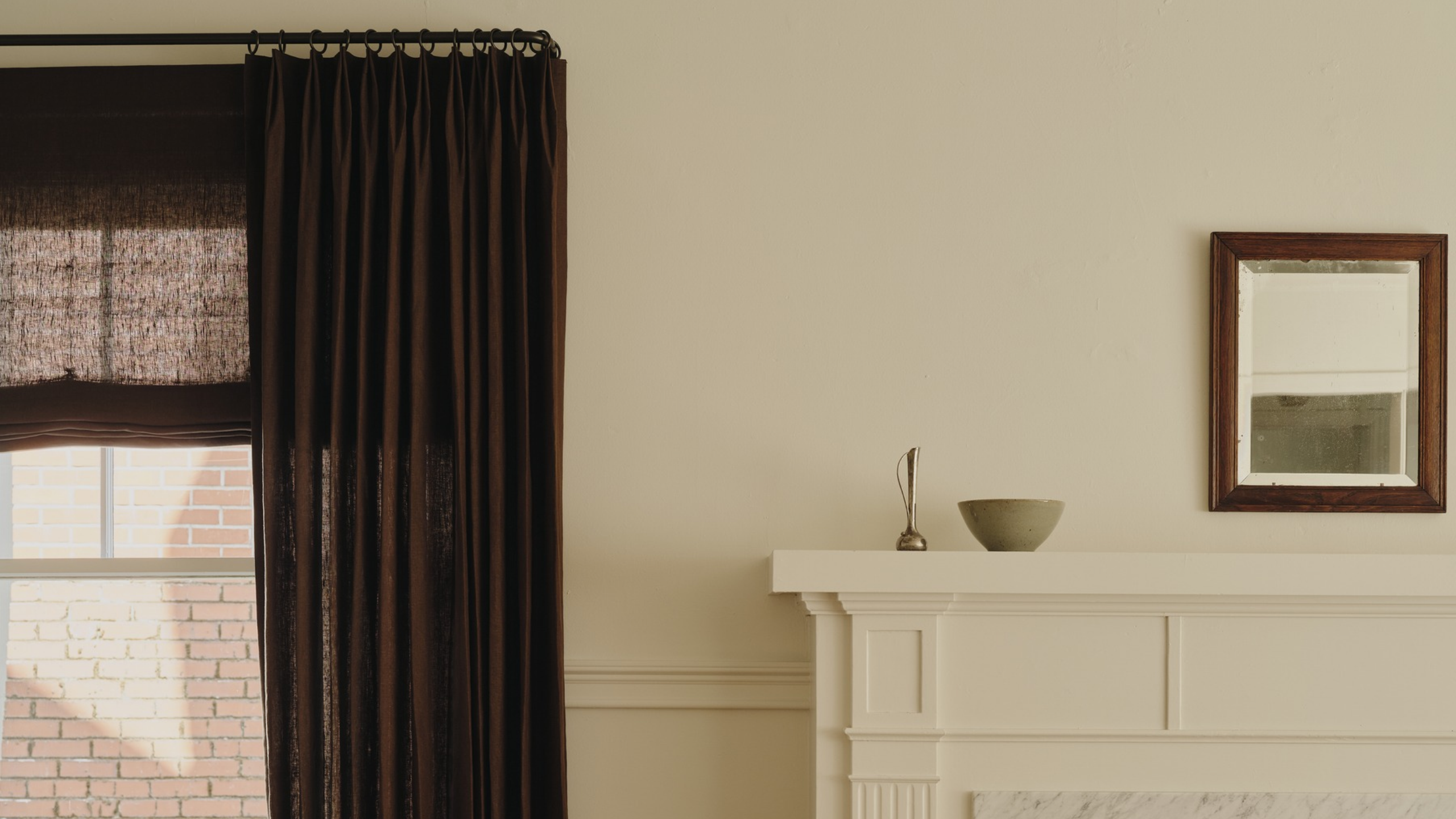 Minimalistisches Wohnzimmer mit einem Kaminsims mit dekorativen Gegenständen, einem rechteckigen Wandspiegel und einer Reihe brauner Vorhänge.